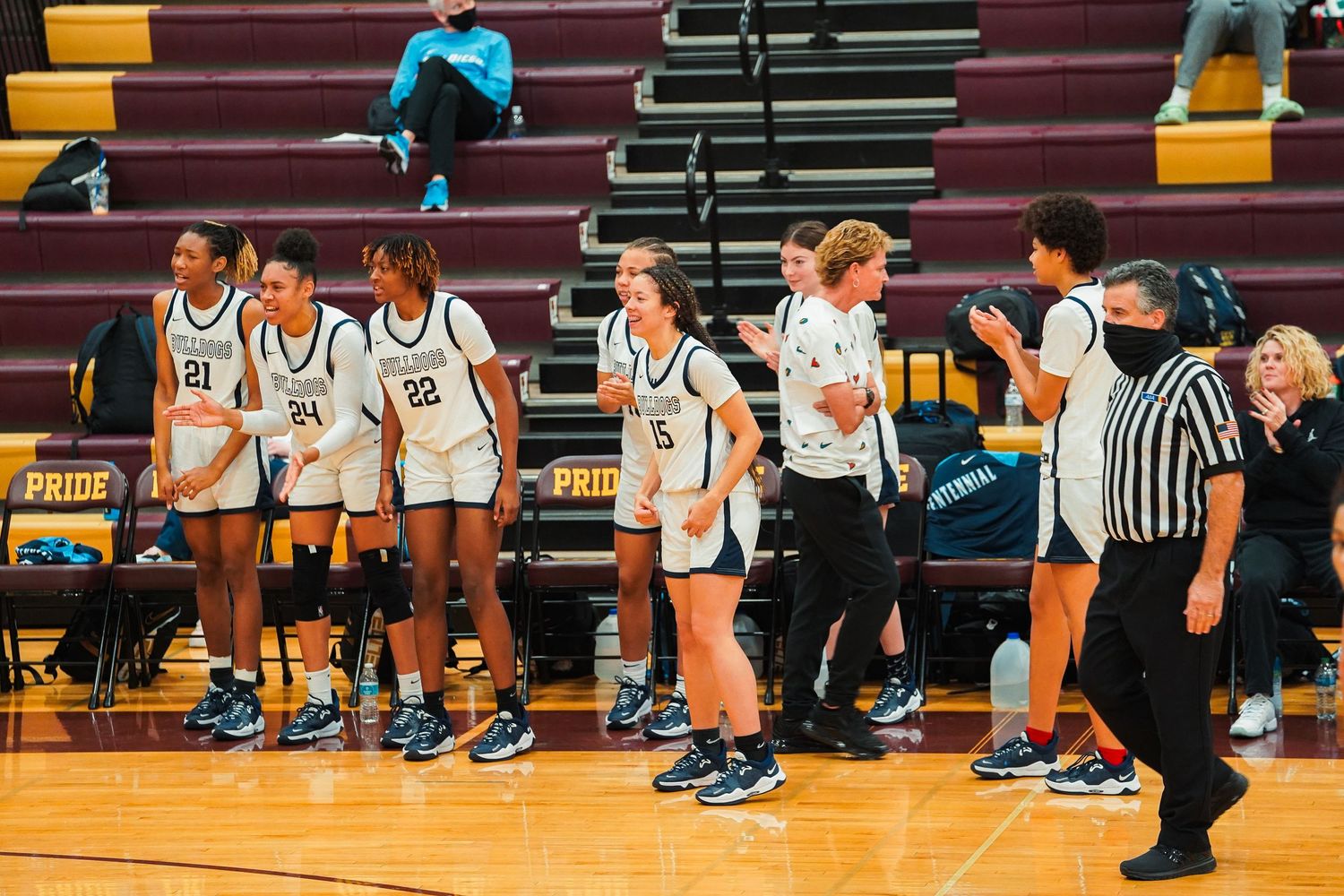 Basketball players and referees gather on court during a game with bleachers in the background.