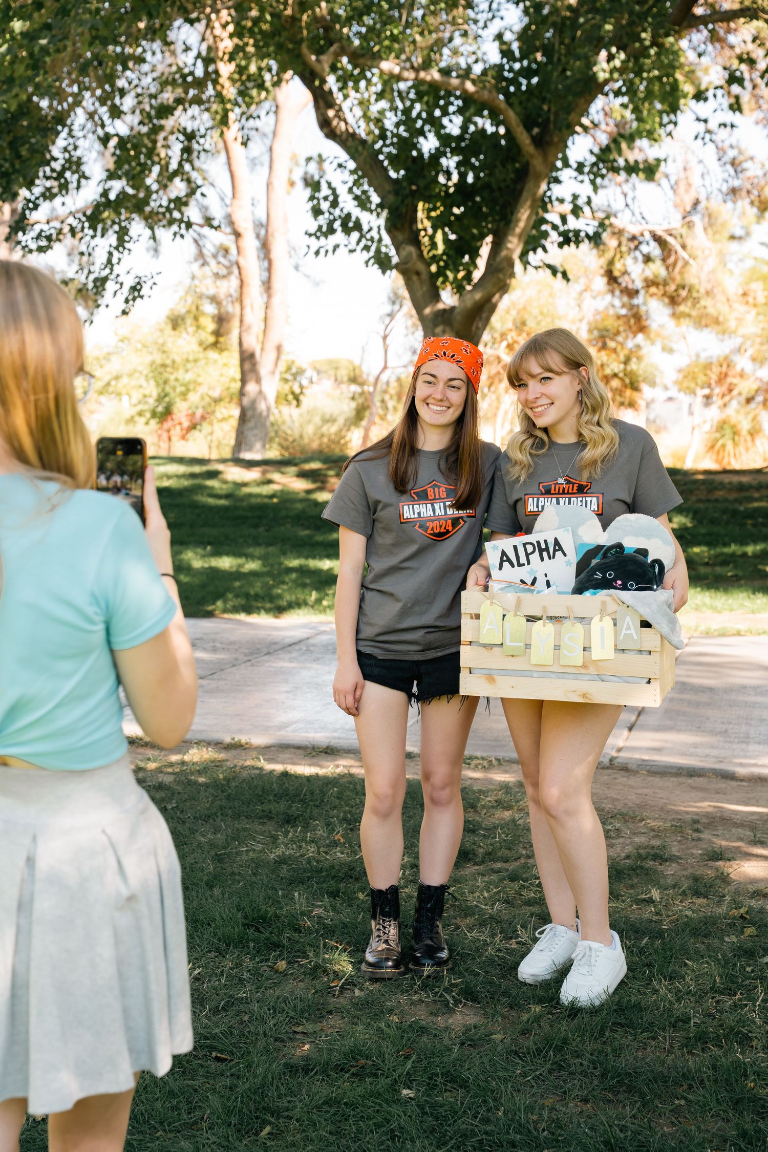 Students pose with craft basket while being photographed on campus pathway.