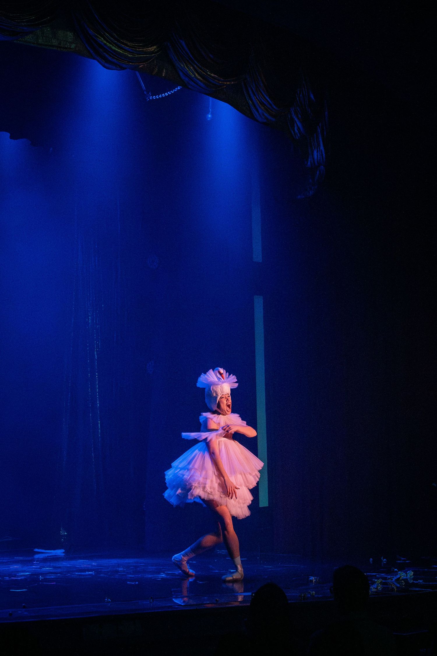 Dancer in flowing pink dress performs dramatic movements under blue stage lighting during theatrical performance.