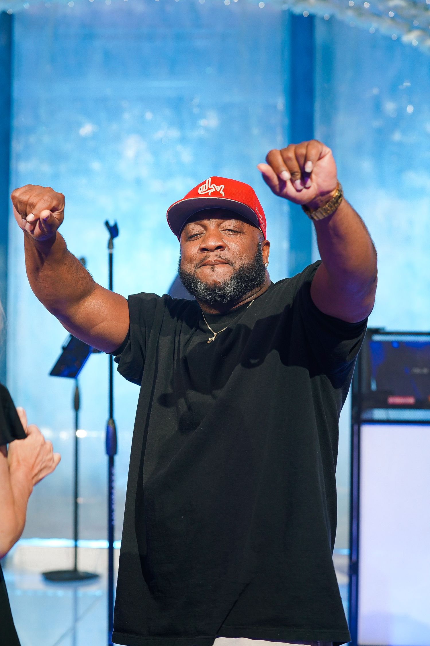 Energetic performer in black shirt and red cap gesturing triumphantly on stage.