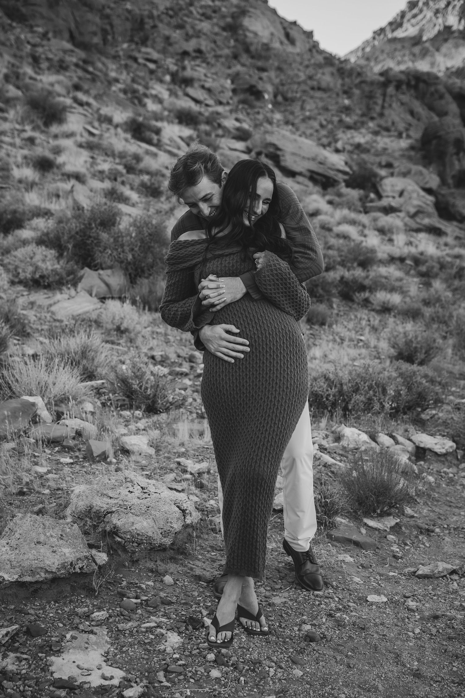 A romantic black and white portrait of a couple embracing on a rocky desert trail.