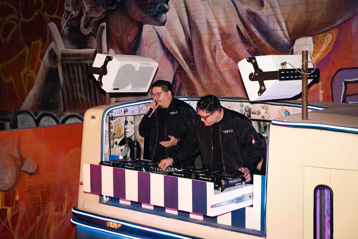 DJs performing from custom vintage-style booth with graffiti backdrop.
