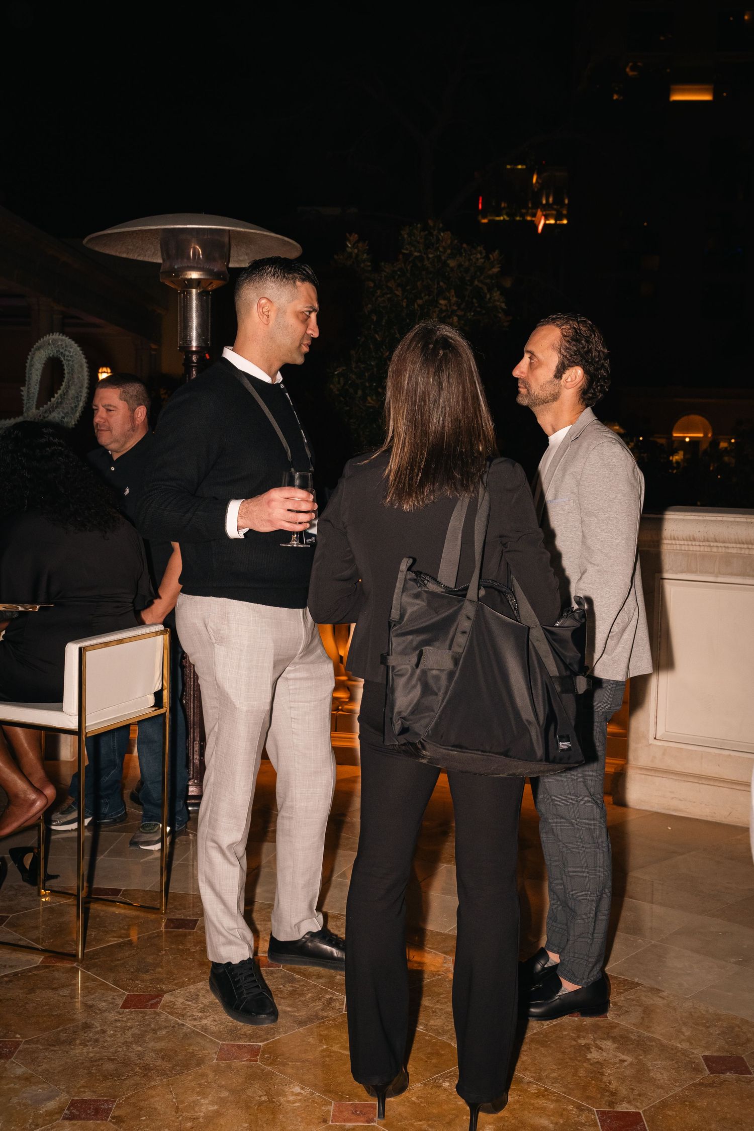 Evening party guests converse in small groups on an outdoor patio.