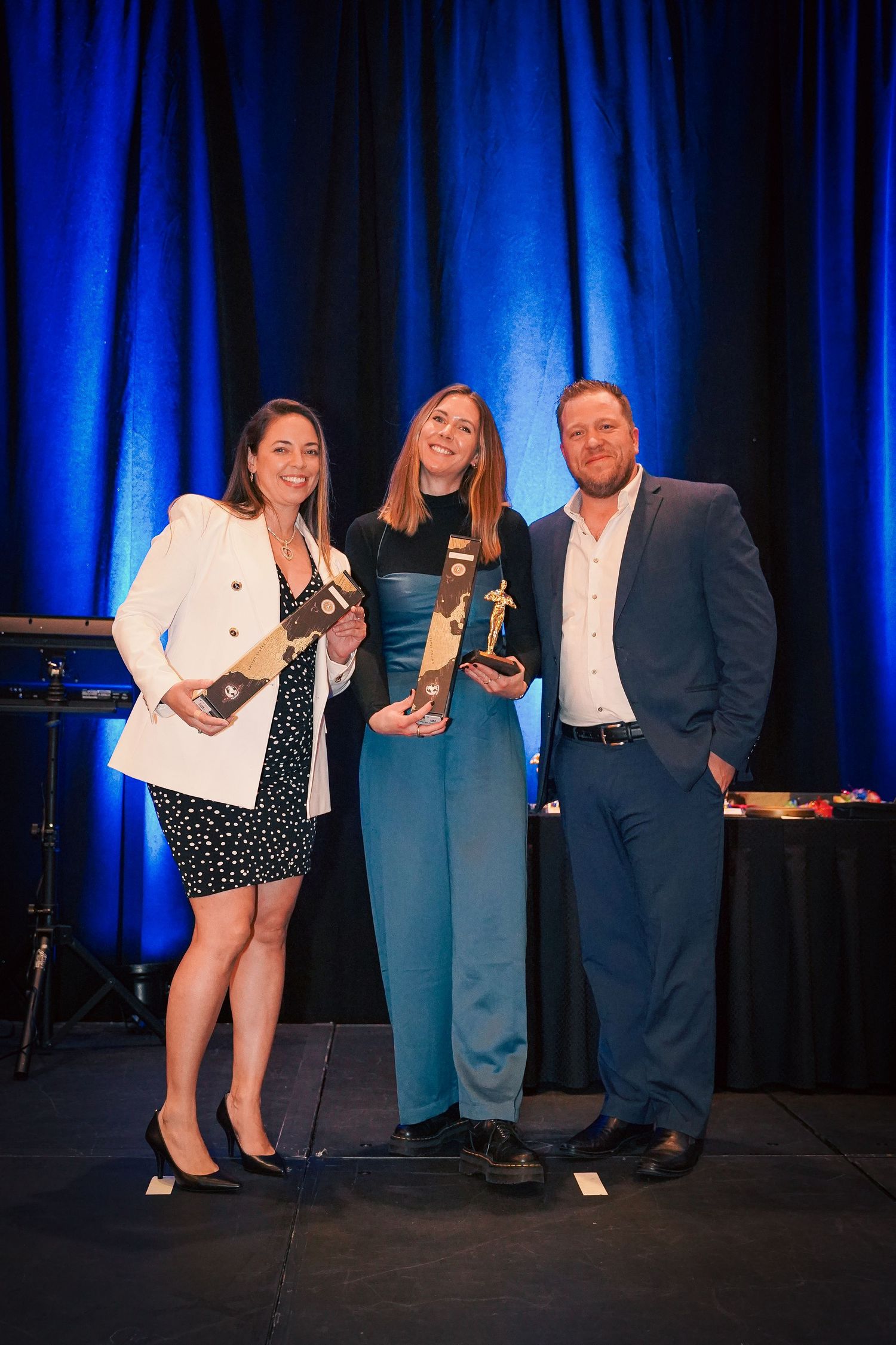 Award winners displaying trophies on stage at corporate ceremony with blue backdrop.