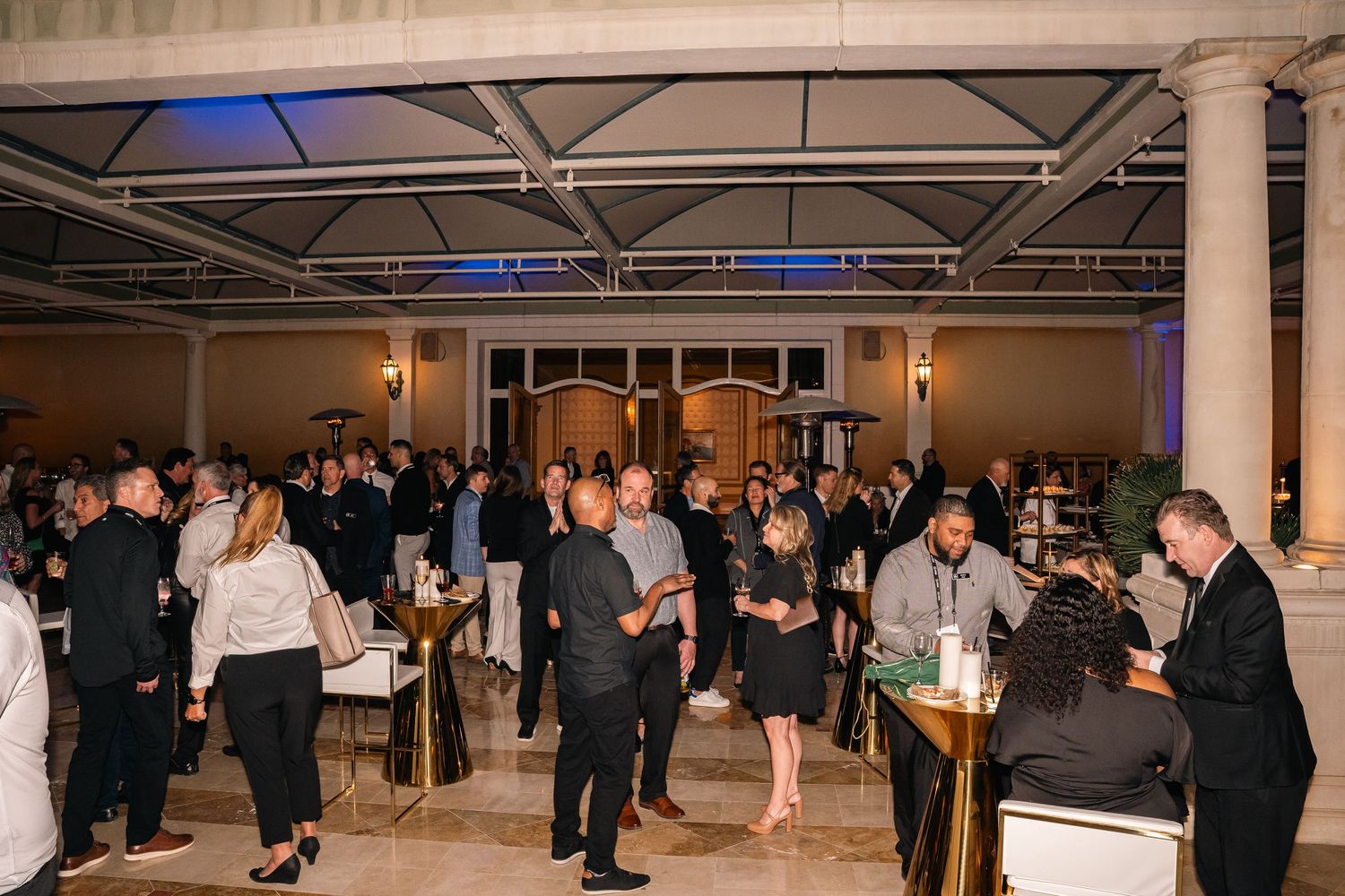 Crowd mingling at elegant corporate networking event with columns and mood lighting.