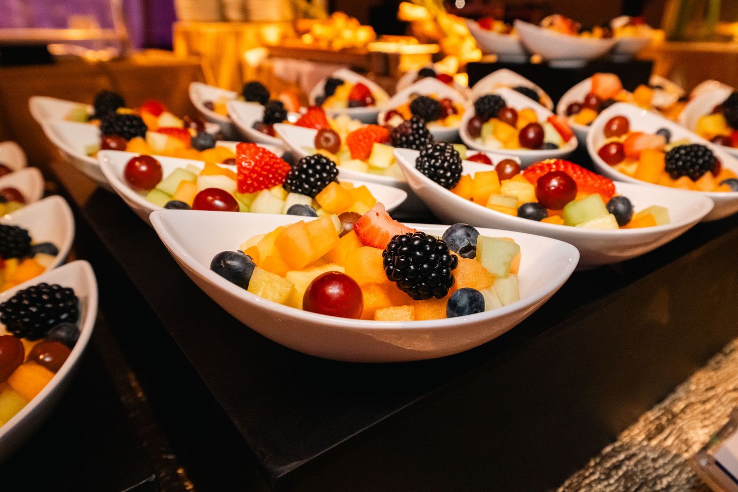 Elegant white spoons filled with fresh berries and fruit arranged in rows for catering service.