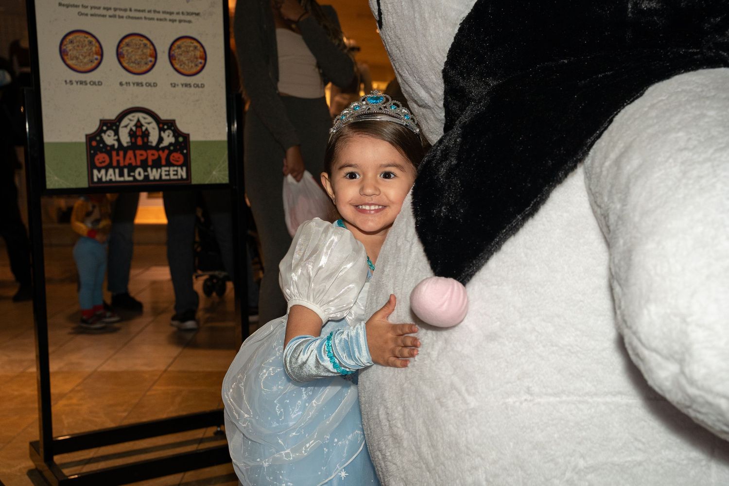 A child in a blue dress interacts with a large white decorative display at a Halloween event.