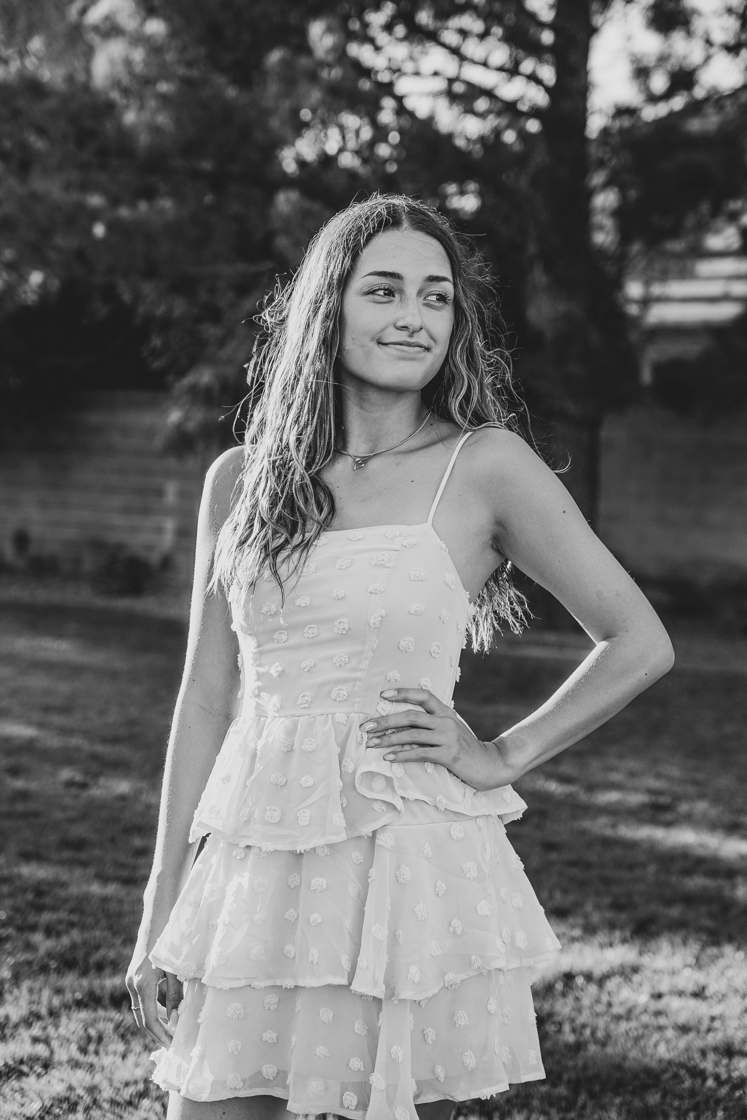 Black and white photo of person in tiered white dress posing outdoors.