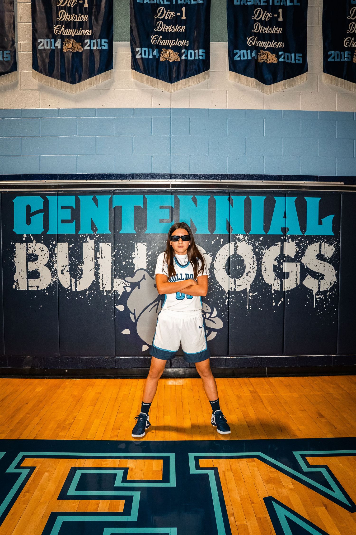Player in white uniform shows athletic stance with basketball in front of team banner.