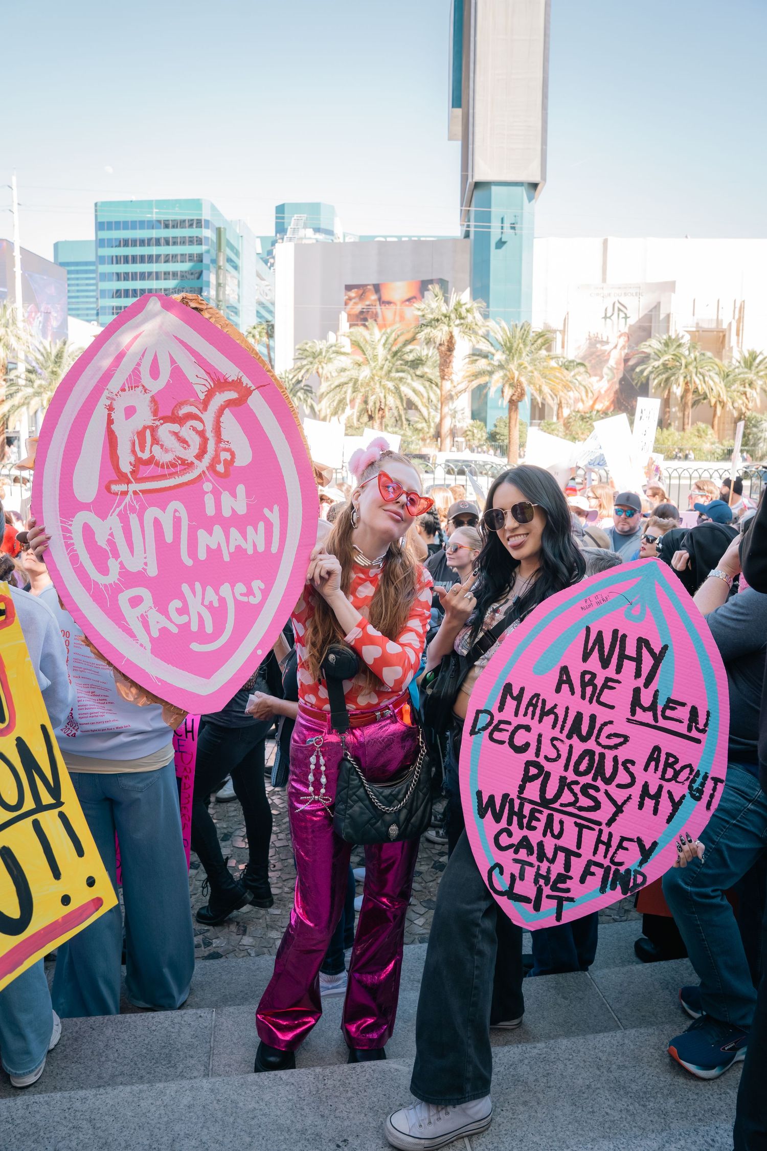 Protesters holding pink heart-shaped signs at a women's rights demonstration in an urban area.