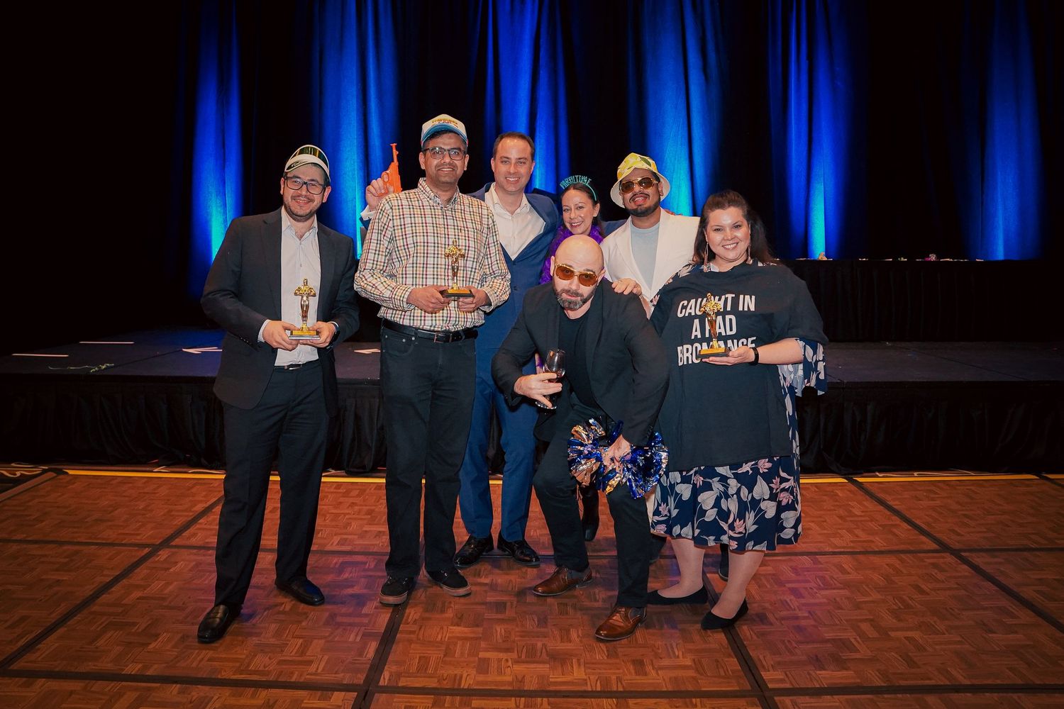 Event attendees pose together in formal attire against a dark backdrop with blue lighting.