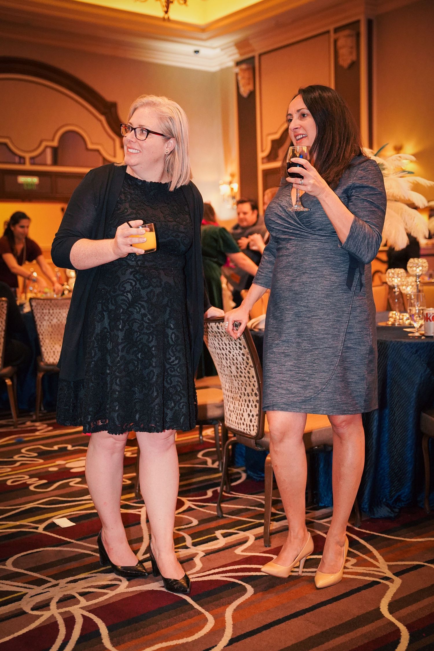 Low angle view of people's legs and feet on a patterned carpet at a formal event.