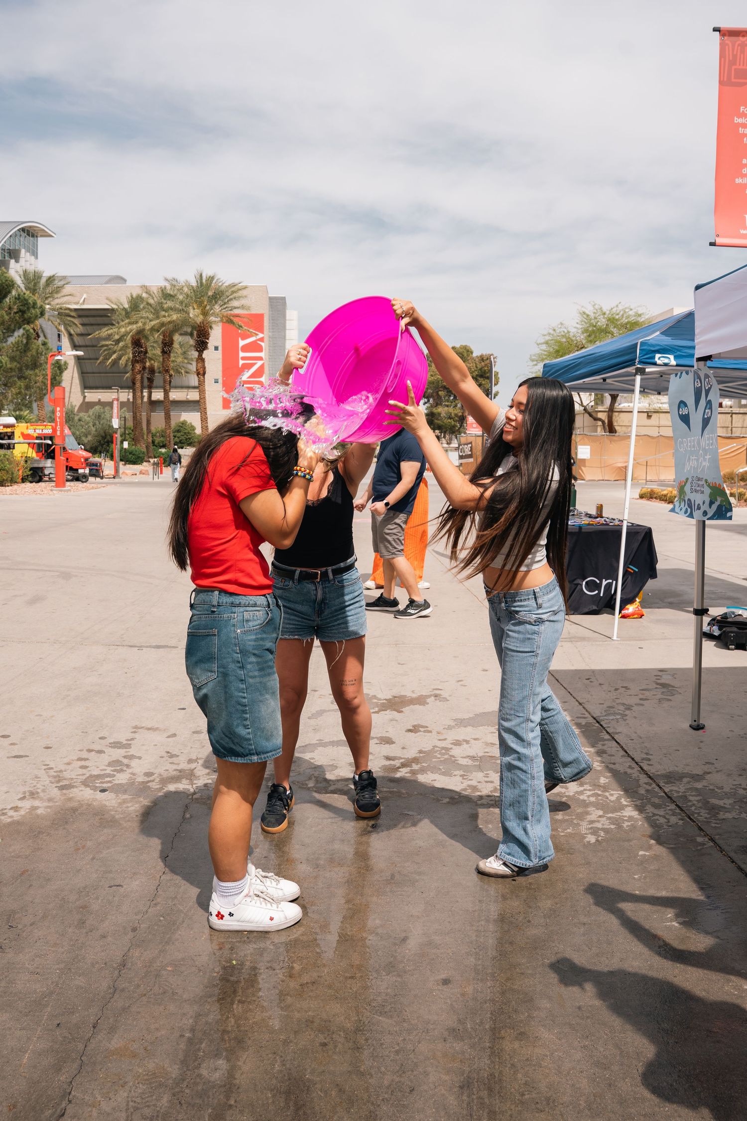 Students having fun pouring pink liquid from a container during an outdoor campus event.