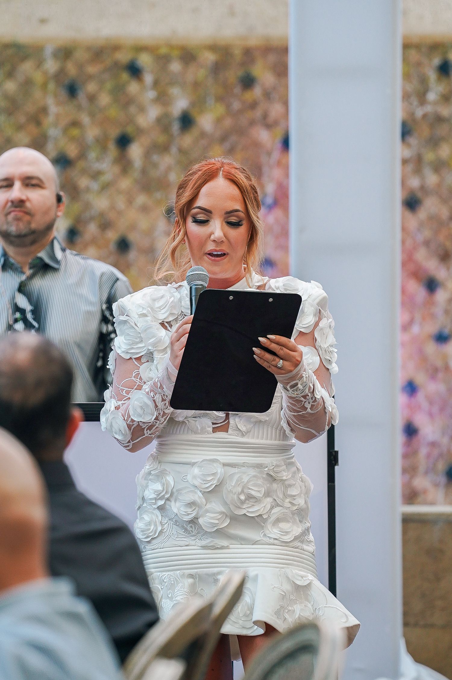 Person in white dress reads from clipboard during outdoor celebration.