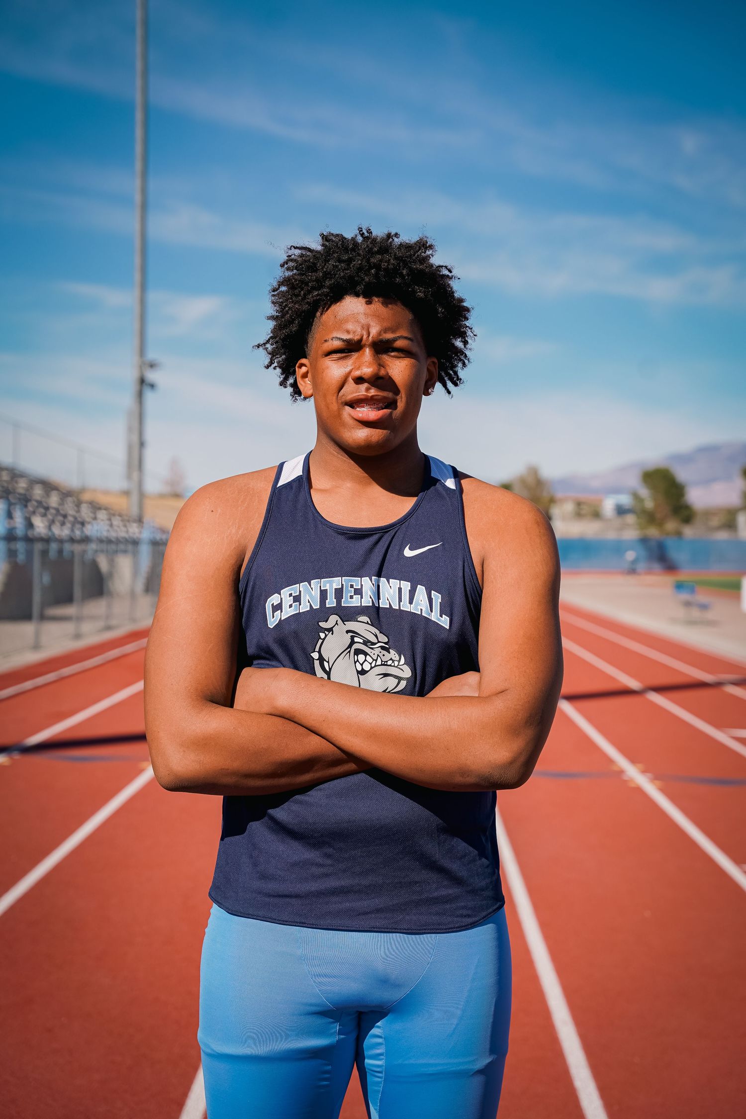 Athlete in navy Centennial team tank and blue shorts poses confidently on outdoor running track.