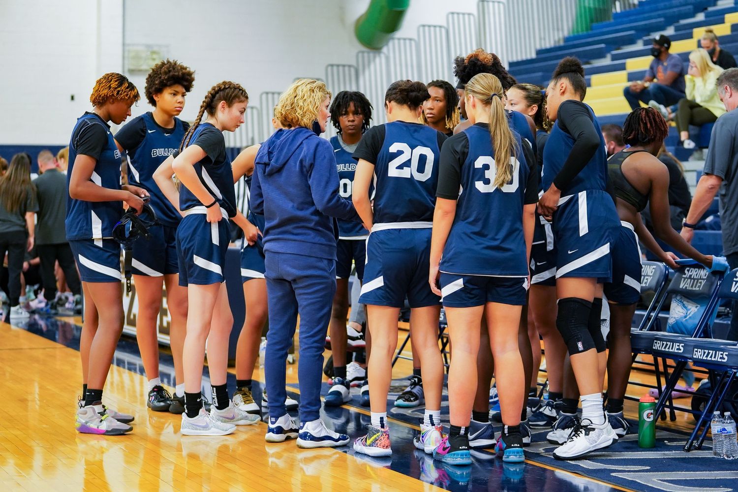 Basketball team huddles together during timeout wearing navy blue uniforms.