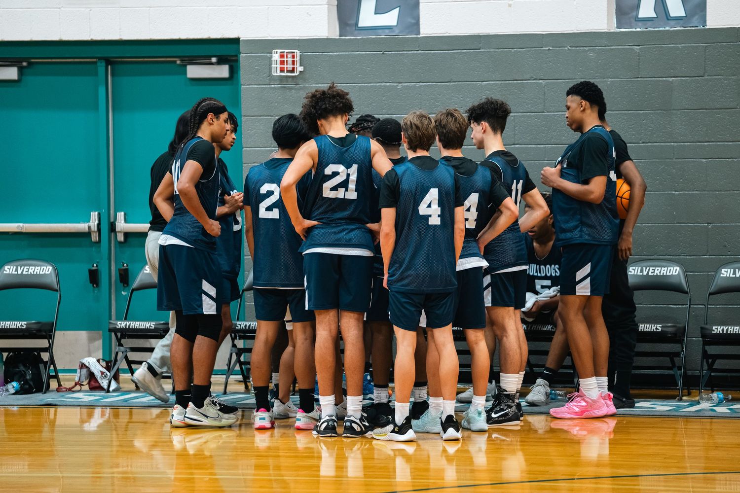 Row of basketball players sitting on bench during game break in gymnasium.