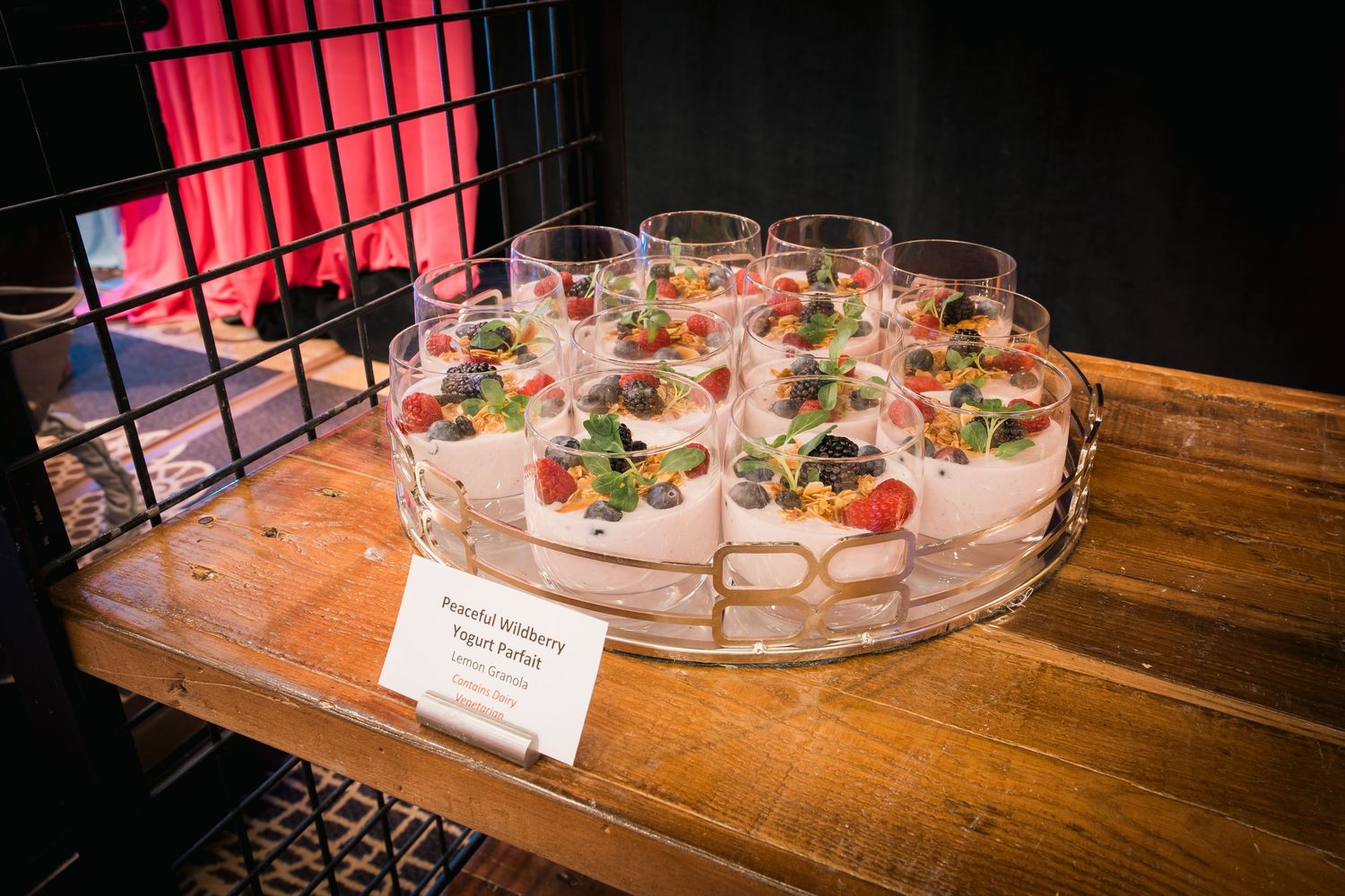 Glass appetizer cups arranged in circular pattern on wooden surface with descriptive place card.