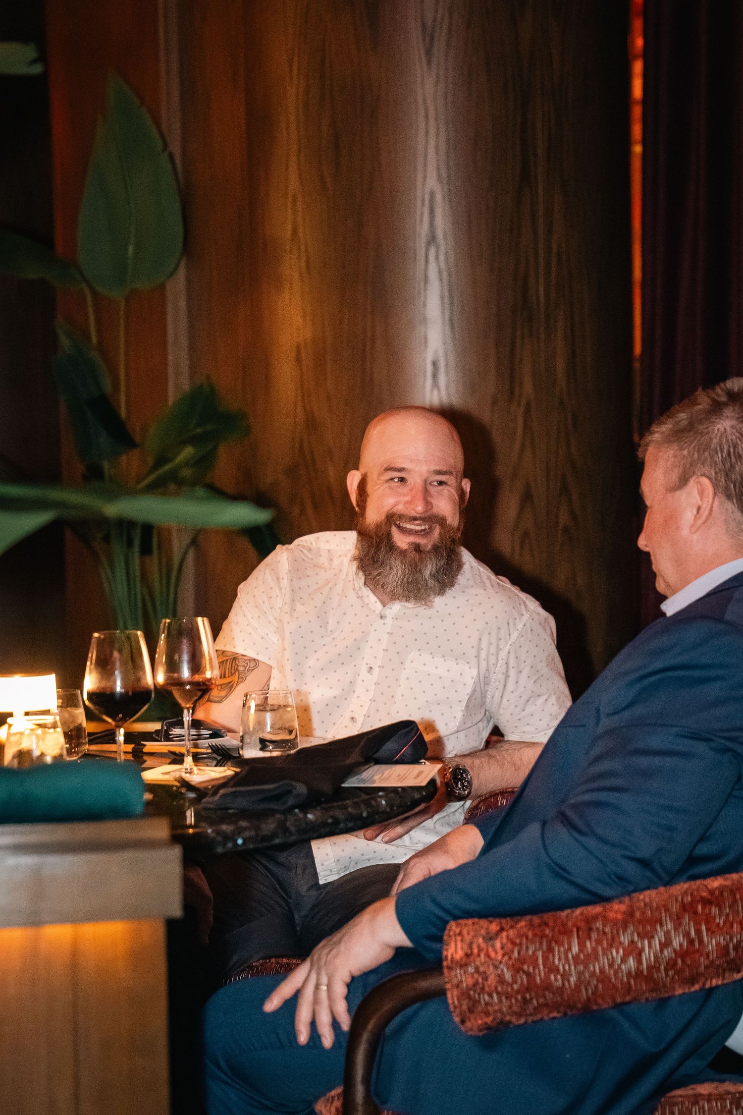 Two guests enjoying wine and conversation at a restaurant table with warm wood paneling.