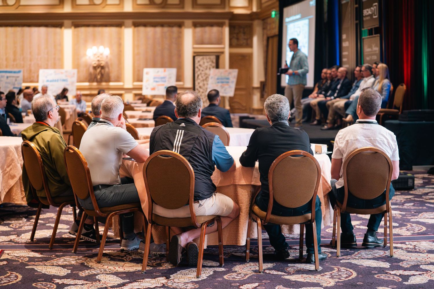 Business professionals seated in rows at a corporate meeting in an elegant ballroom.