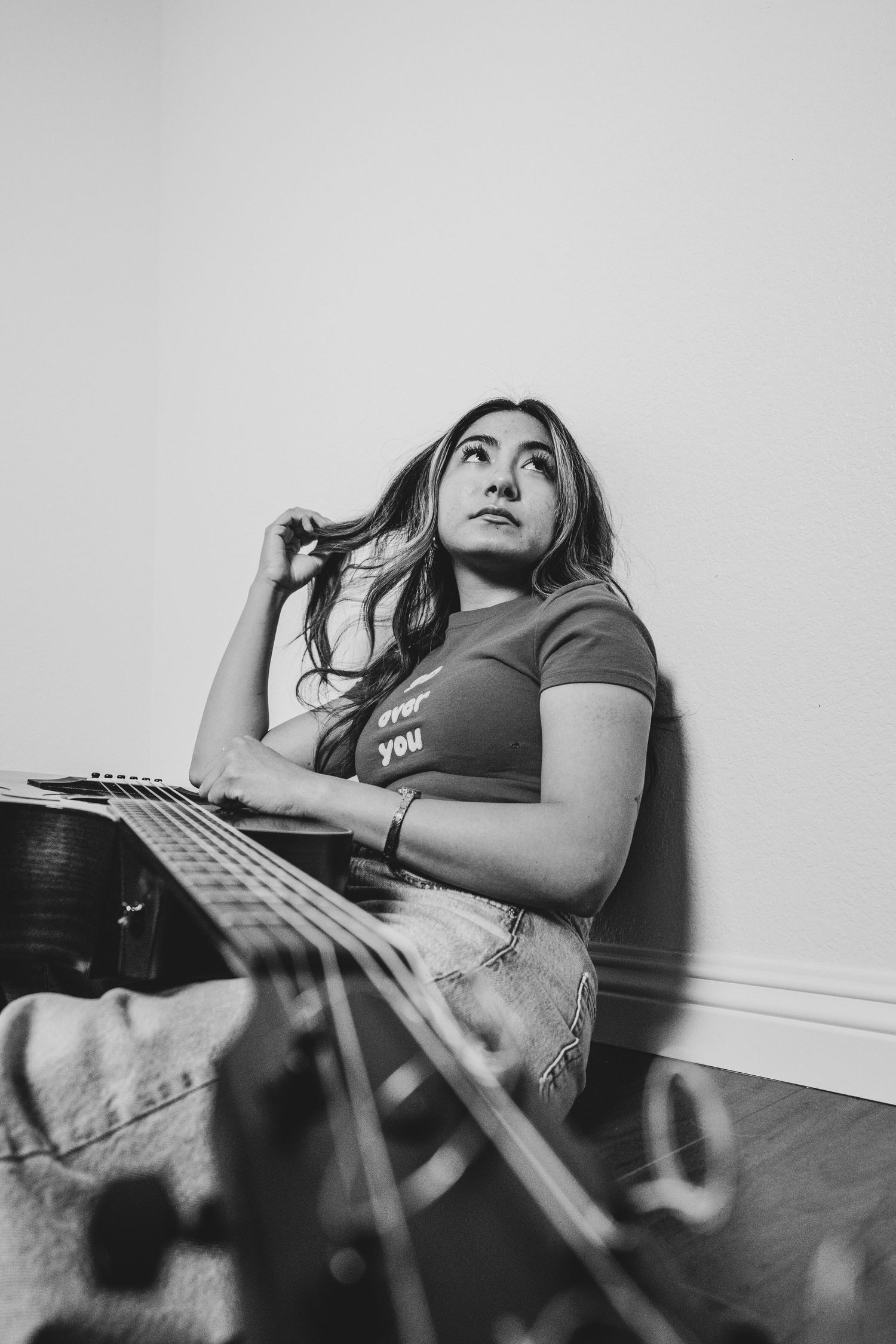 Black and white artistic portrait of someone sitting on floor playing electric guitar while looking up pensively.
