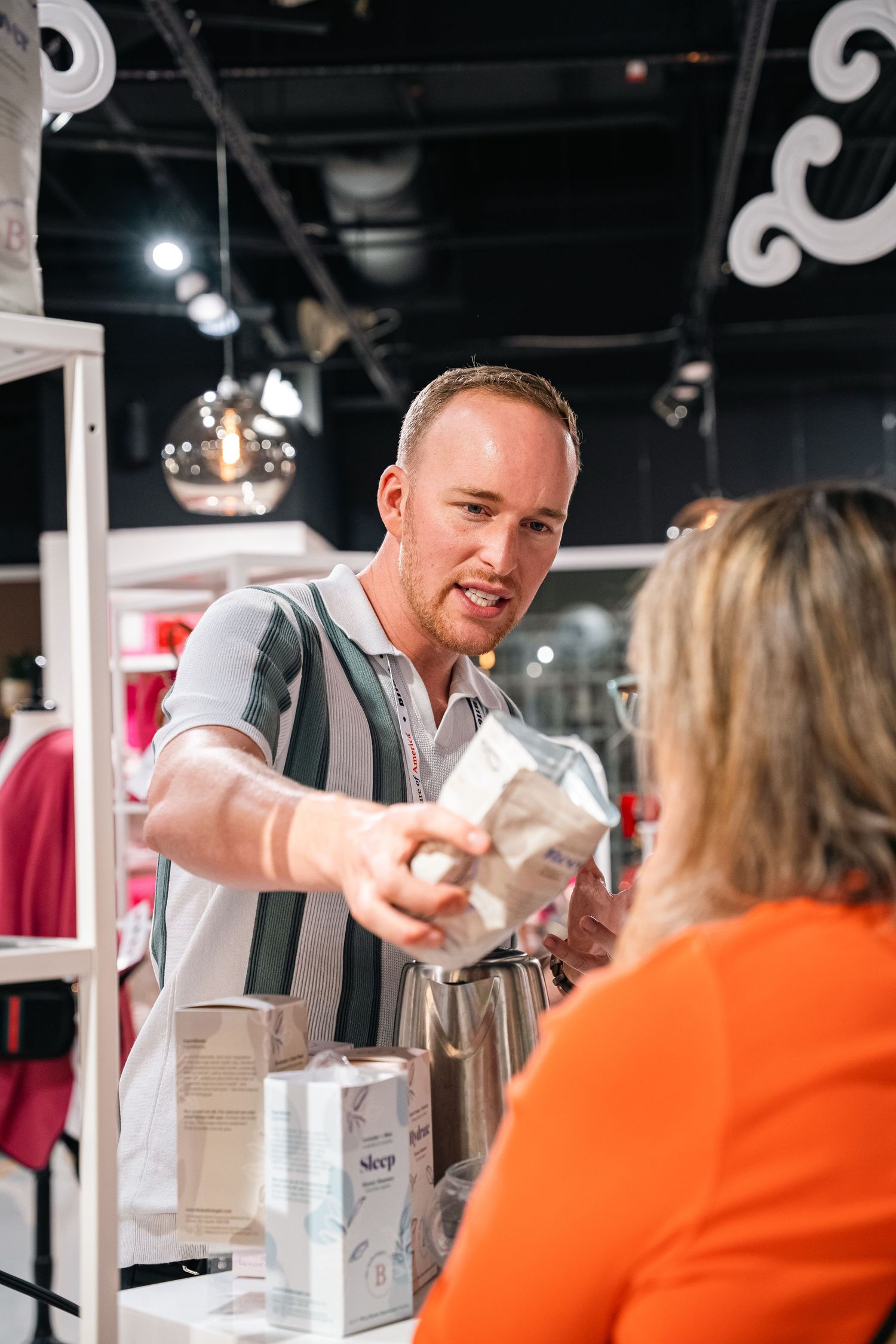 Retail worker in suspenders hands product to customer at modern store counter.
