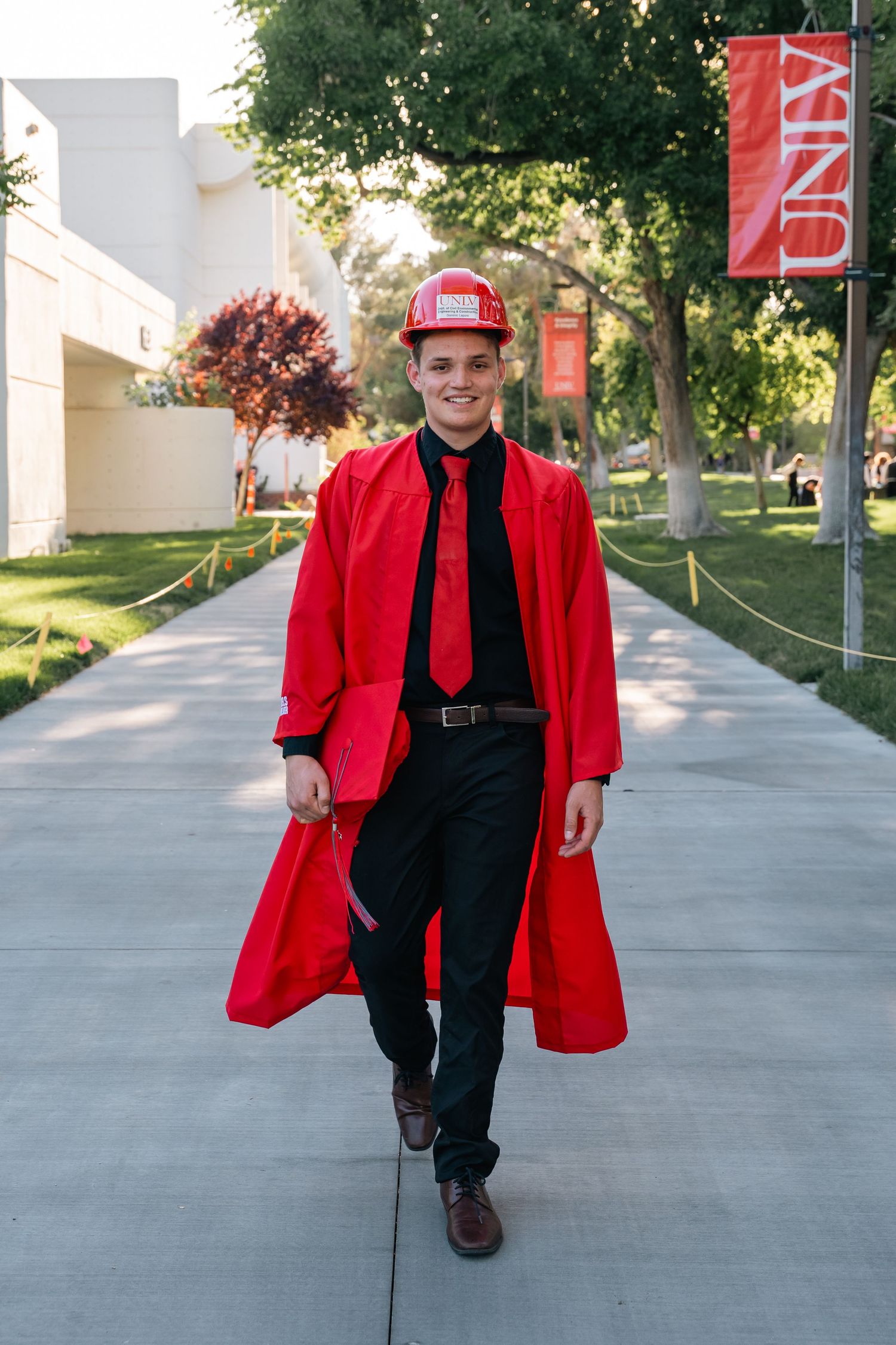 Graduate walks along campus pathway wearing red graduation gown and cap.