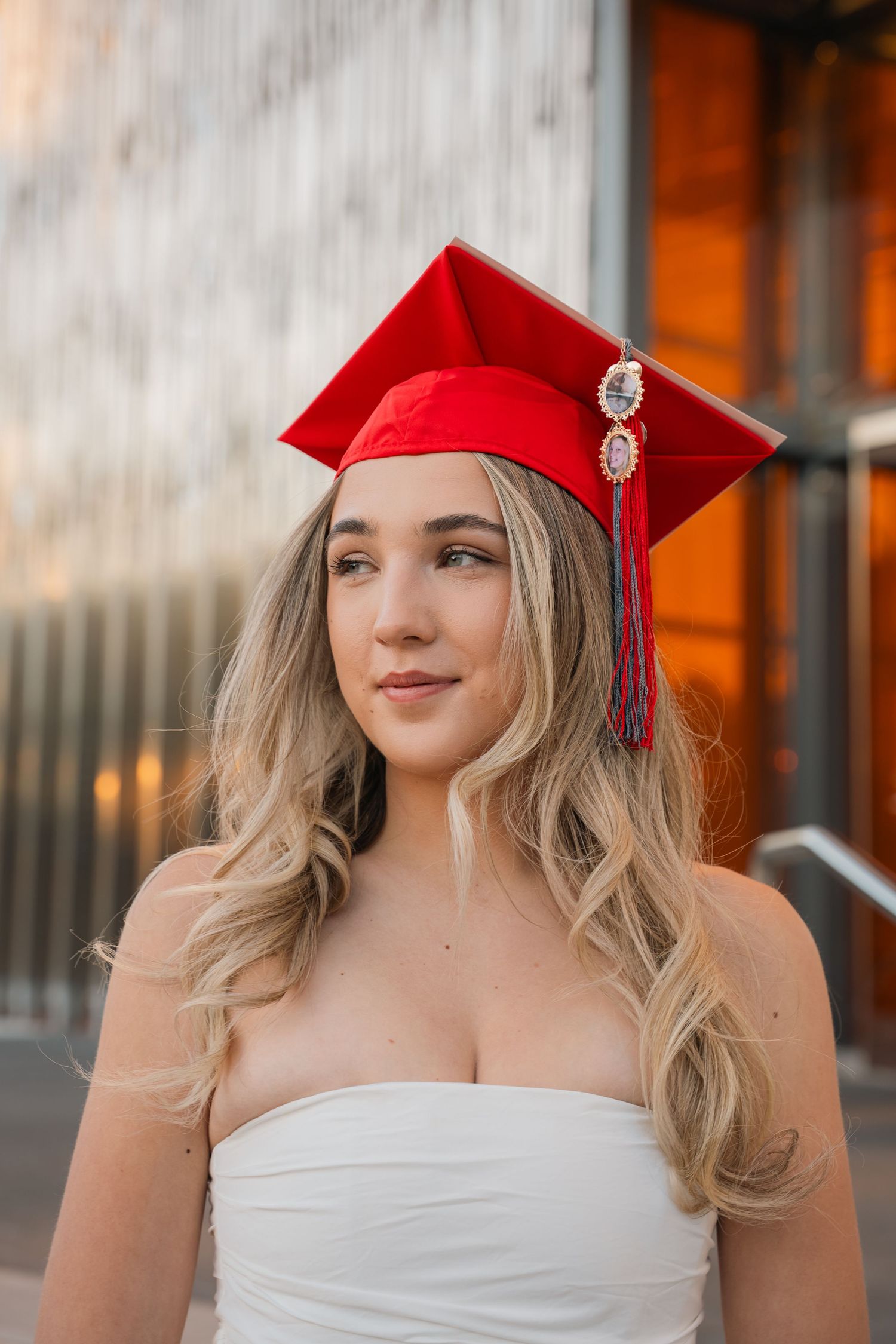 Graduate in red cap with decorative tassels poses during golden hour photo session.