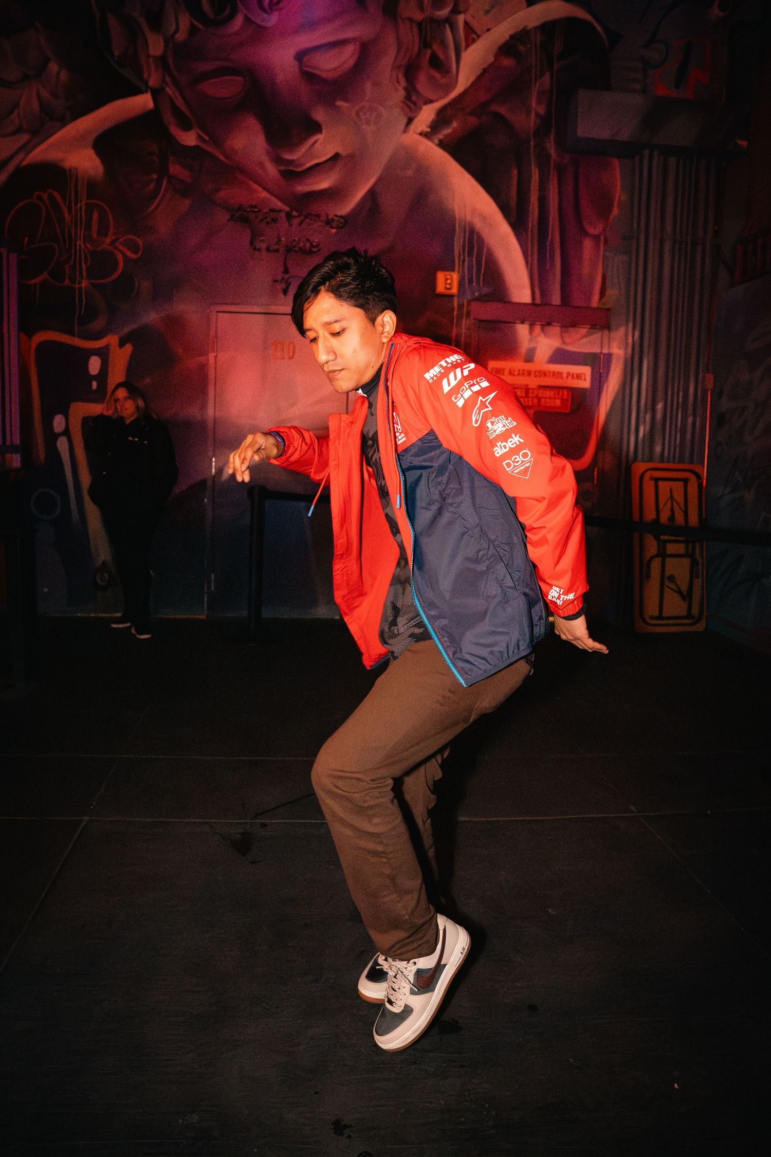 Dancer in red jacket performing against a dark backdrop with decorative wall art.
