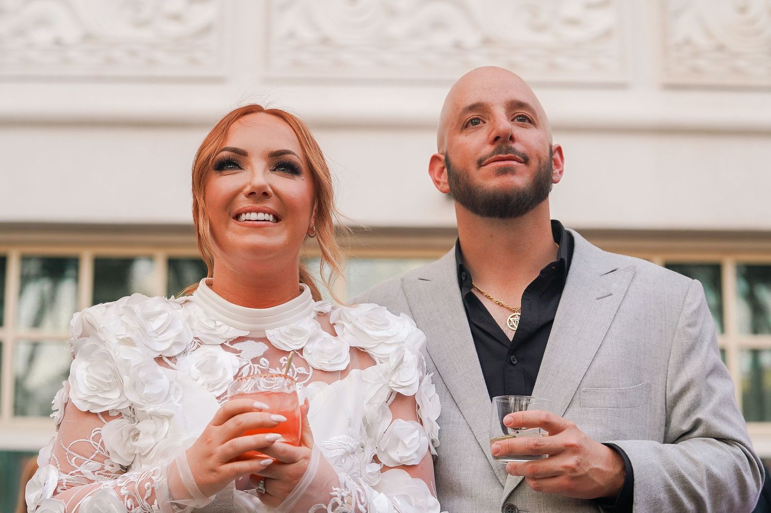 A well-dressed couple enjoying drinks at an elegant venue with ornate white ceiling details.