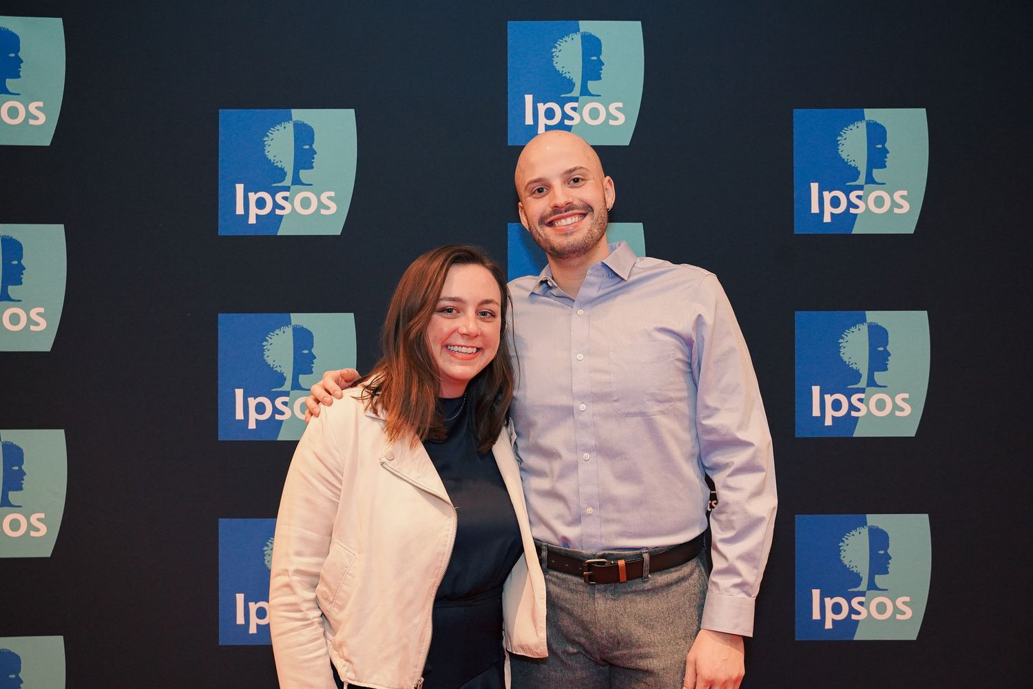 Professional photo of two people standing in front of Ipsos branded backdrop.