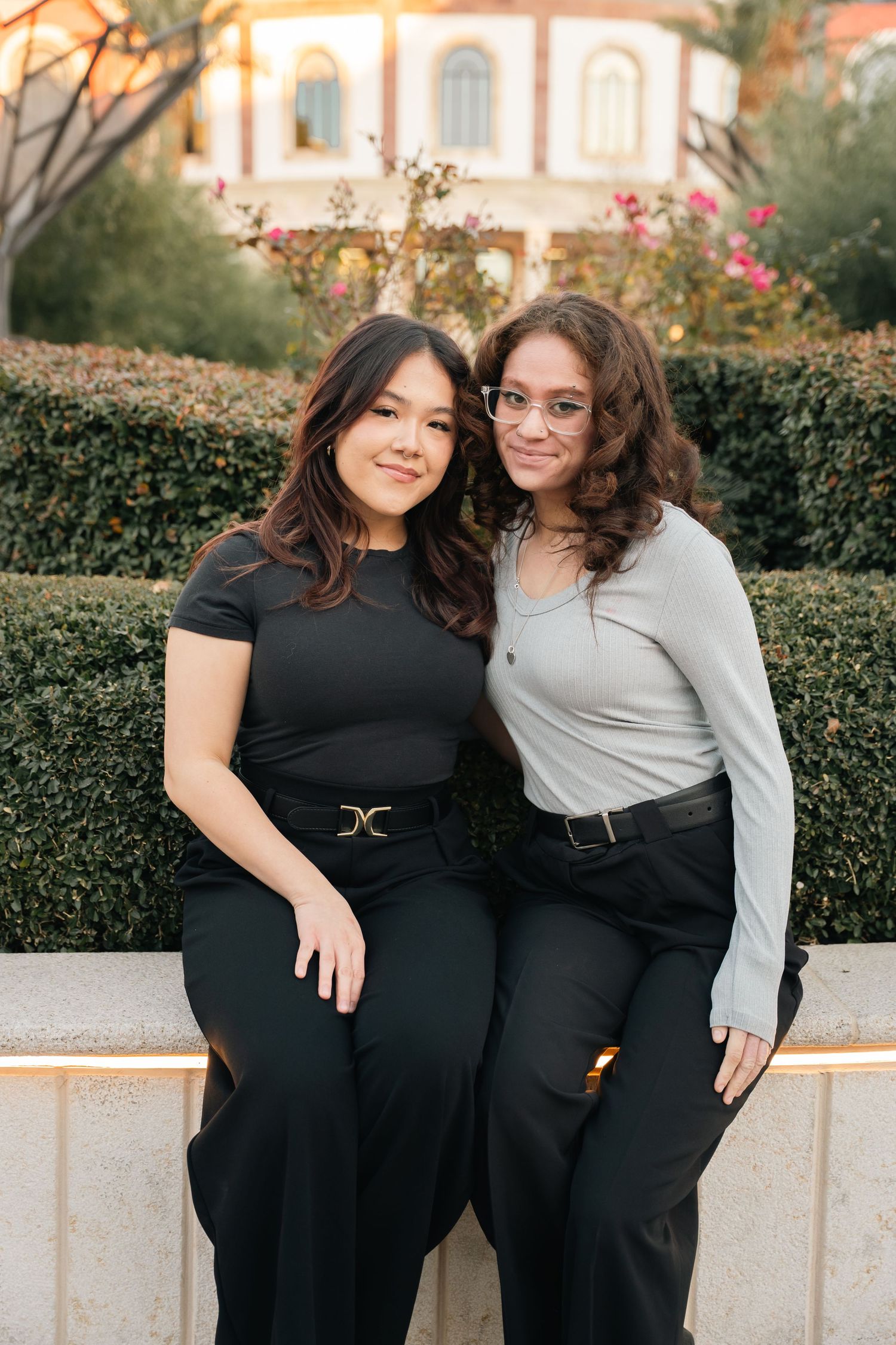 Two friends sitting together on a stone bench with a decorative building facade in the background.