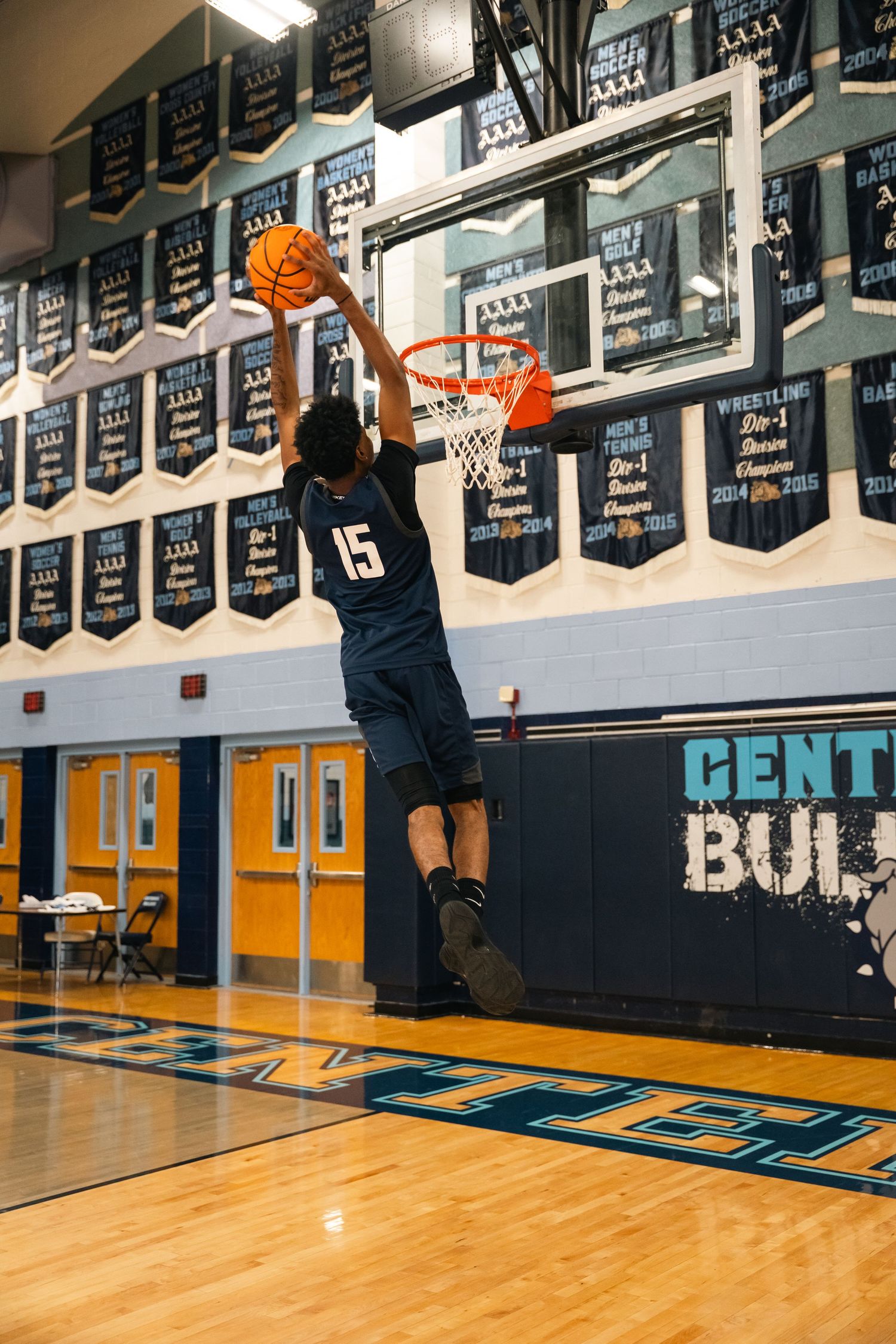 Player in navy jersey number 15 performing slam dunk under championship banners.