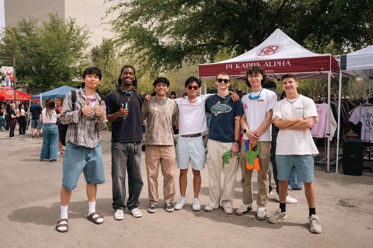 Group of students posing together at outdoor campus event with tents.