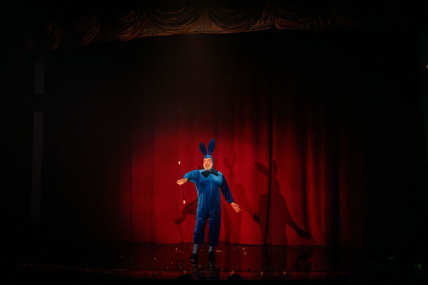 Silhouetted performer dances on stage with dramatic red lighting and curtains.