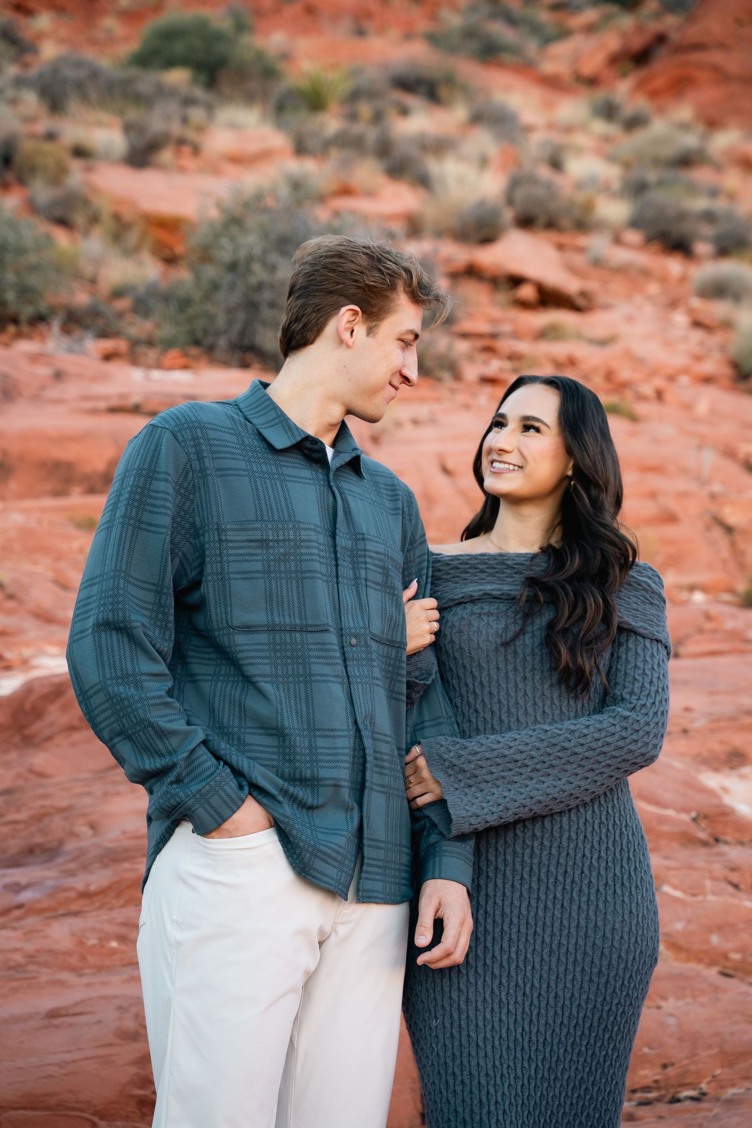 A loving couple in coordinated outfits sharing a tender moment among red rocks.