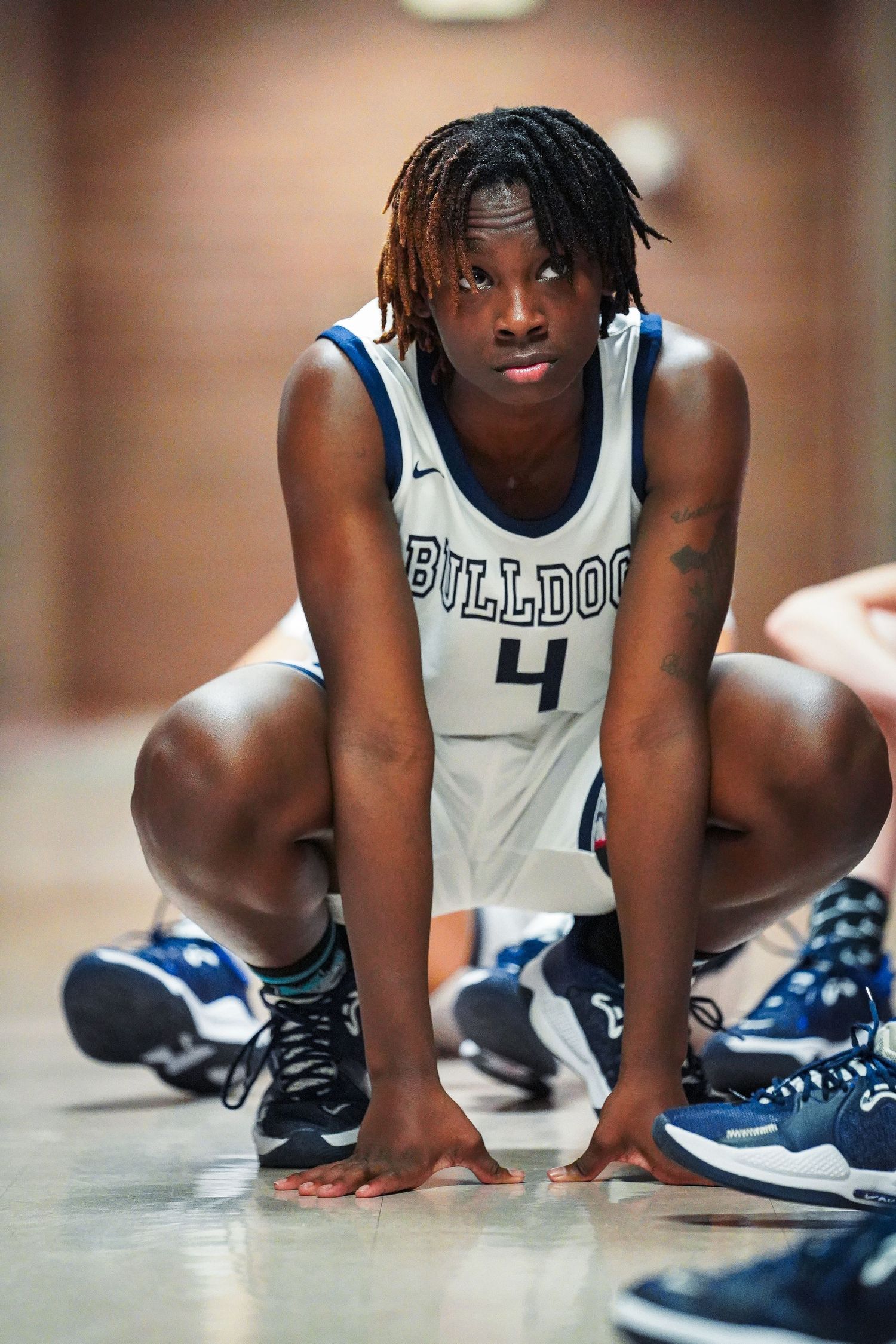 Basketball player in Bulldog uniform crouches on floor during game.