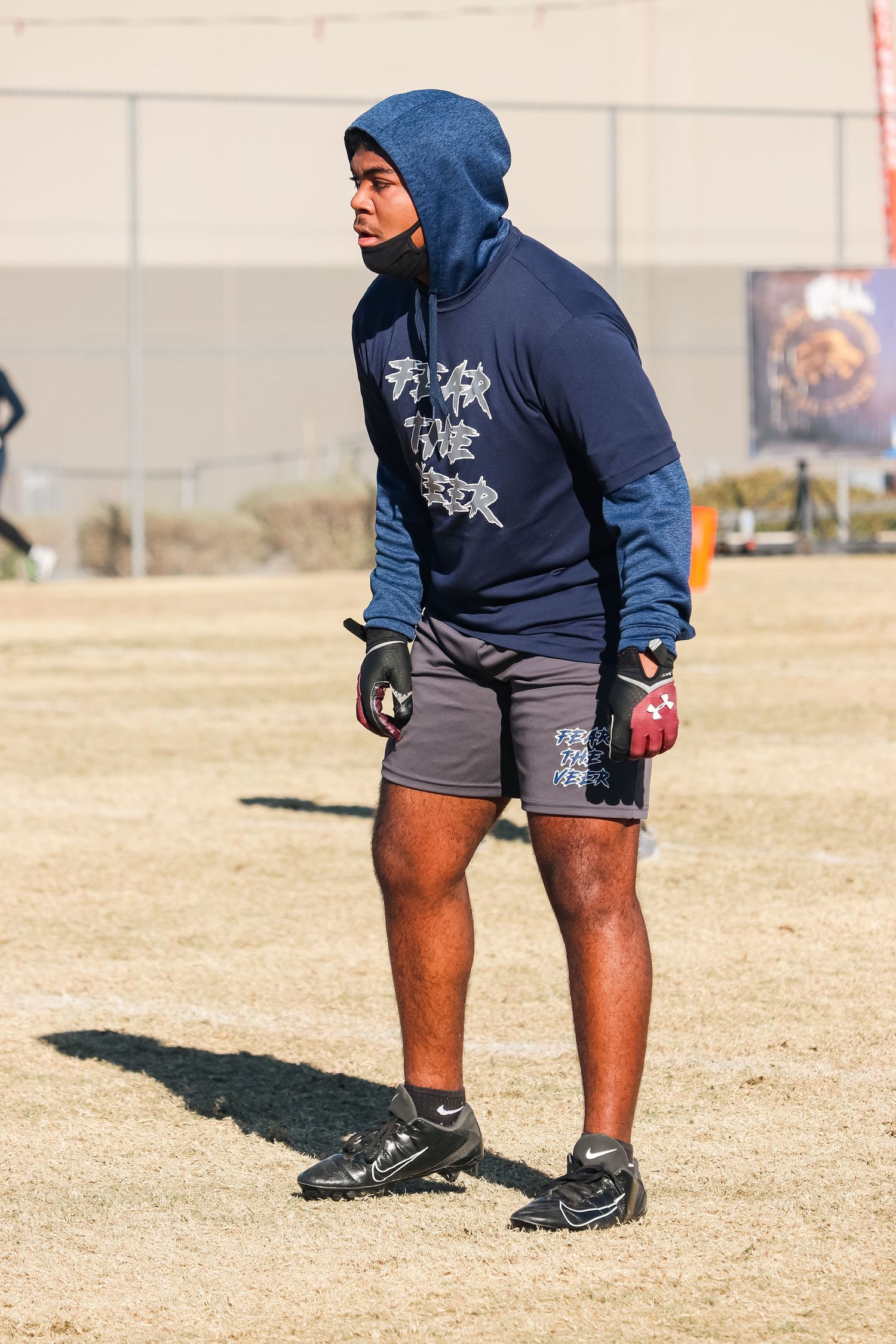 A player in a navy hoodie and gray shorts stands on a sports field.