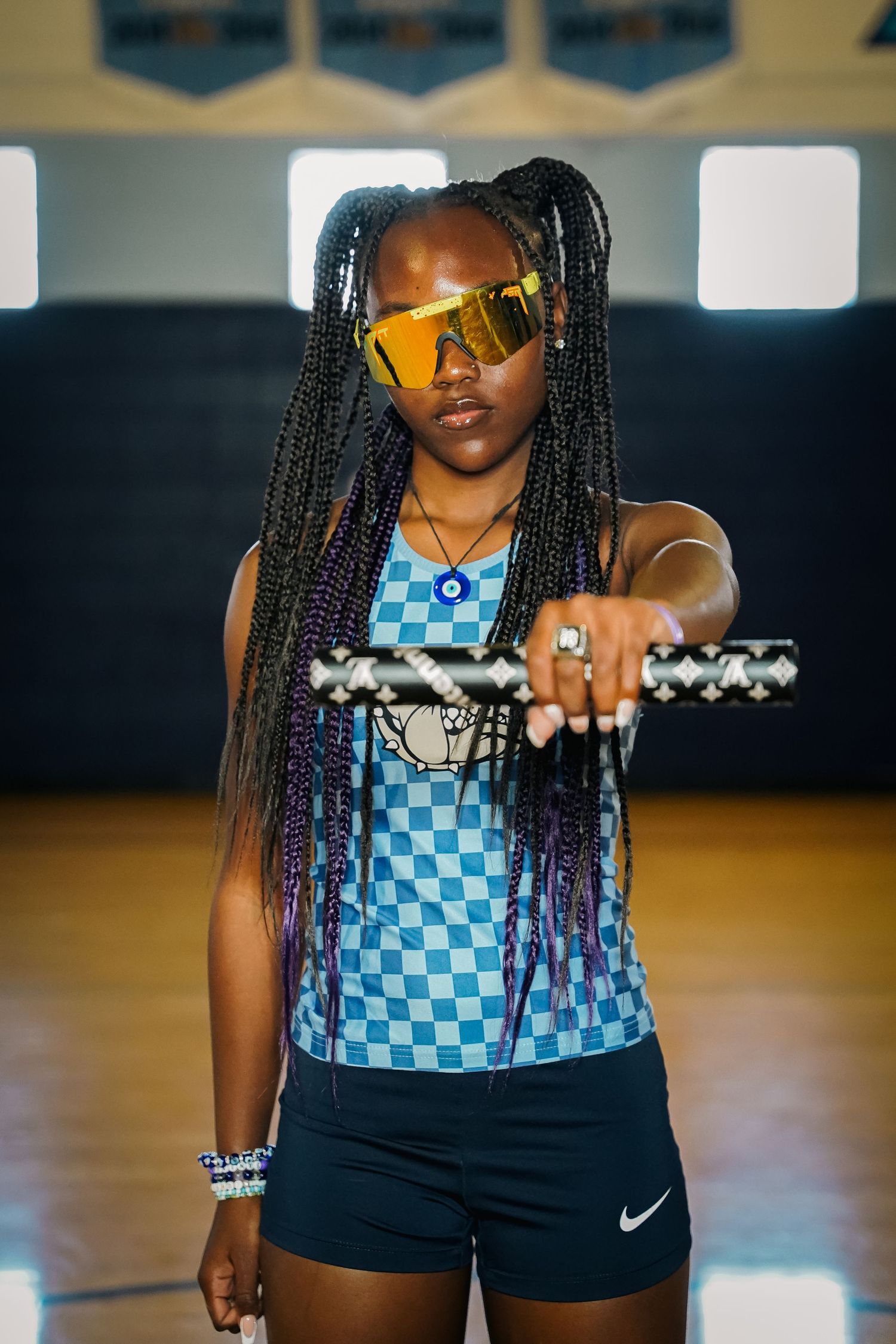Athletic model wearing yellow sunglasses and checkered blue uniform poses in indoor gym setting.