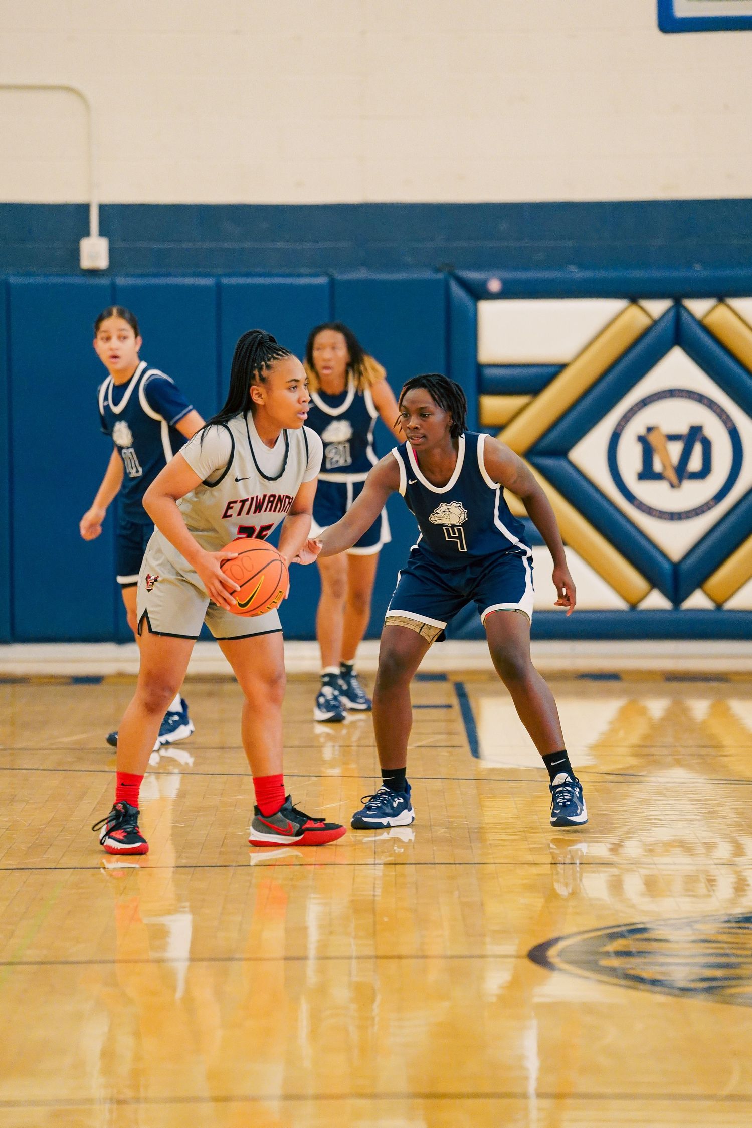 Players in navy and white uniforms crouch in defensive positions during basketball game.
