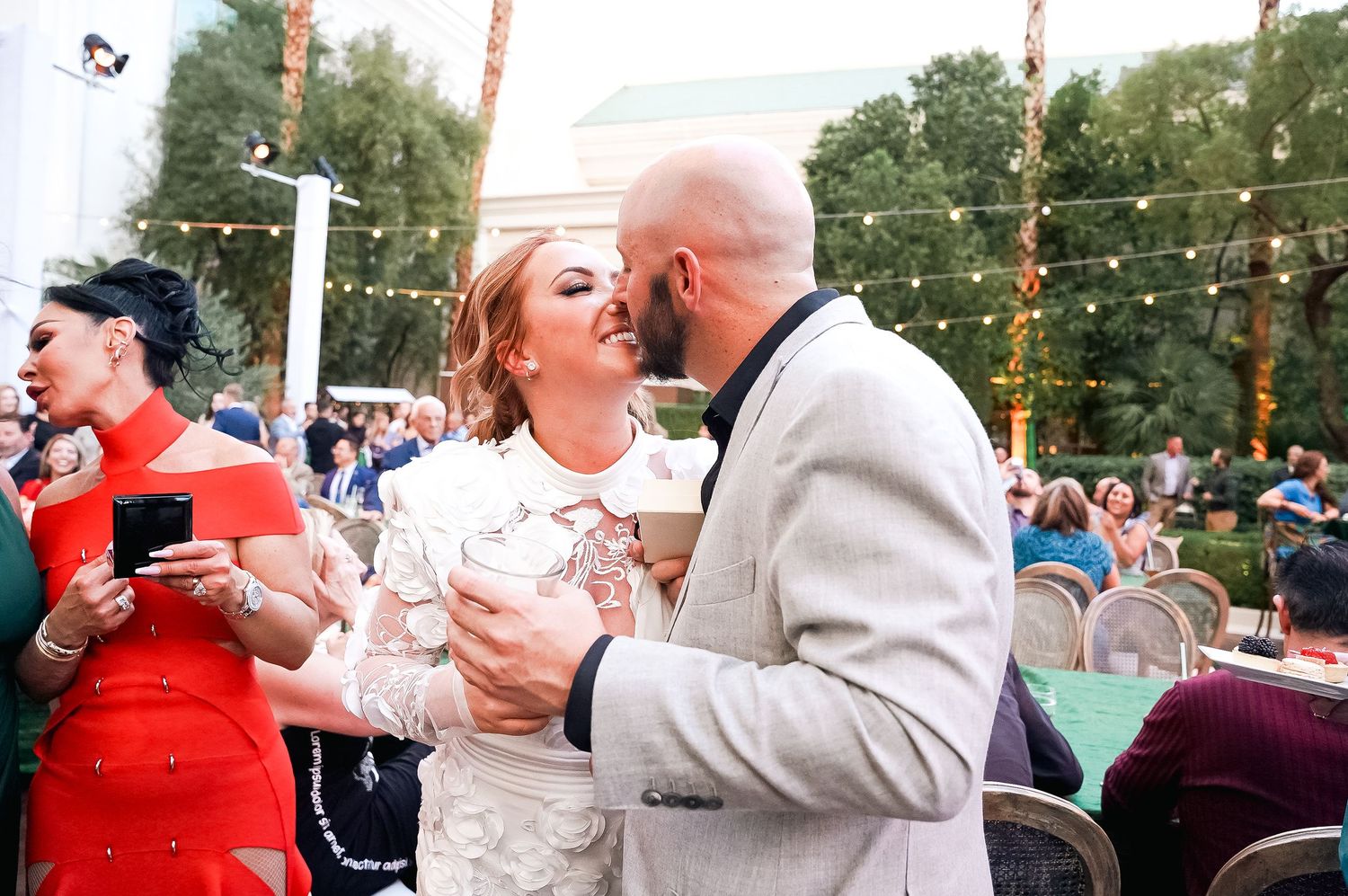 Outdoor wedding reception with string lights and palm trees at sunset.