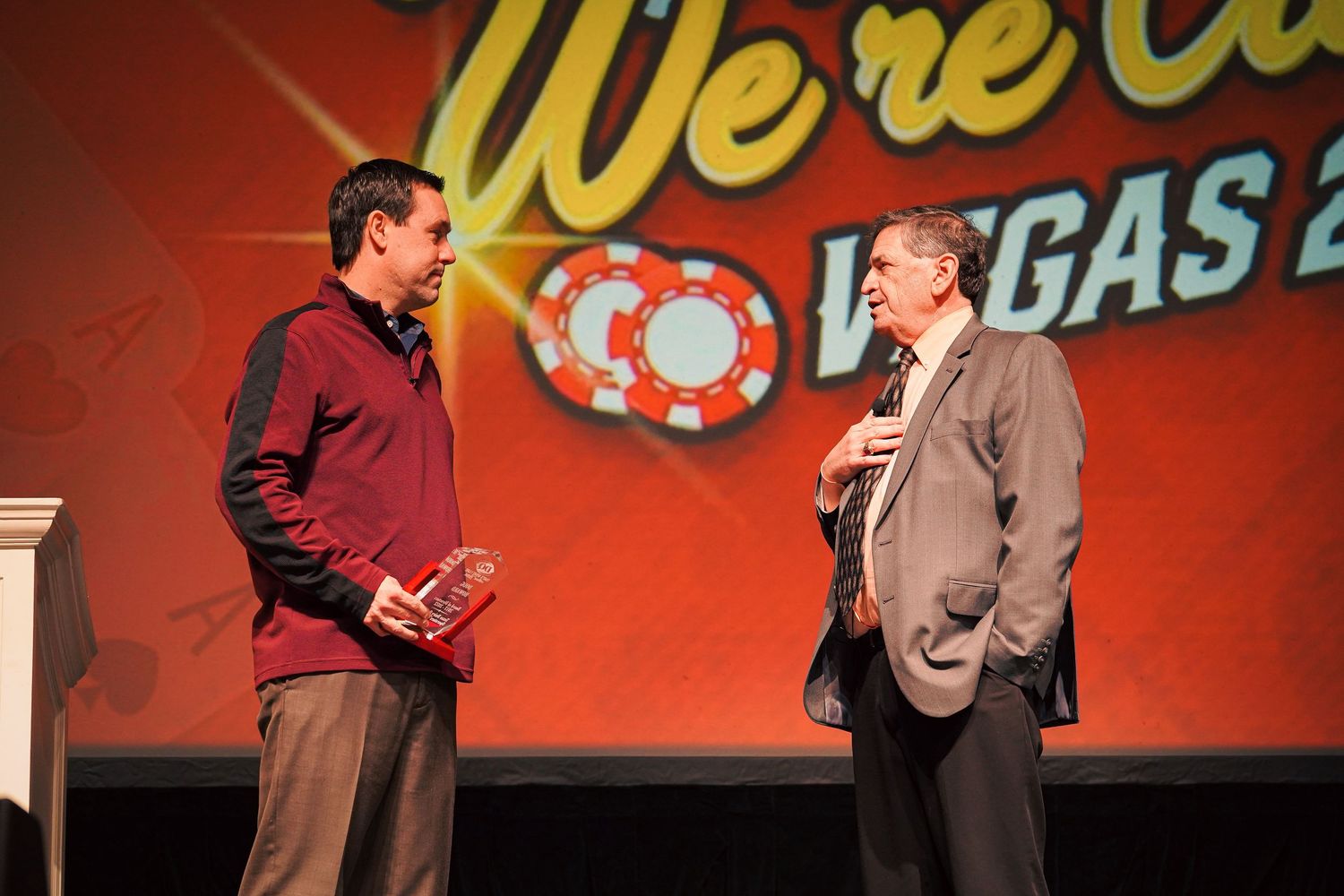Two speakers conversing on stage with red Vegas-themed backdrop.