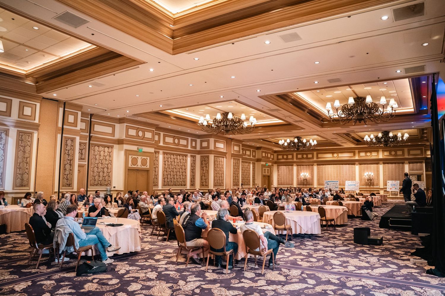 Elegant ballroom setup with attendees seated at round tables during professional conference.