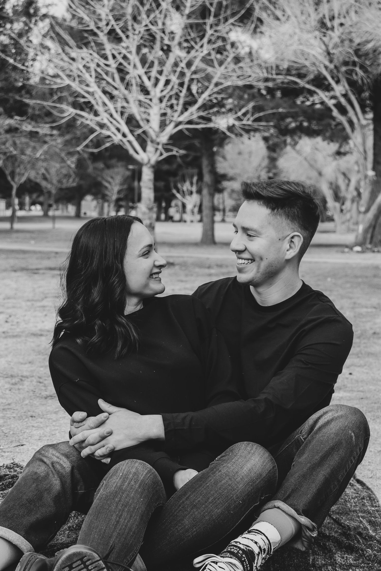 Black and white portrait of a couple sitting and laughing together in a park.