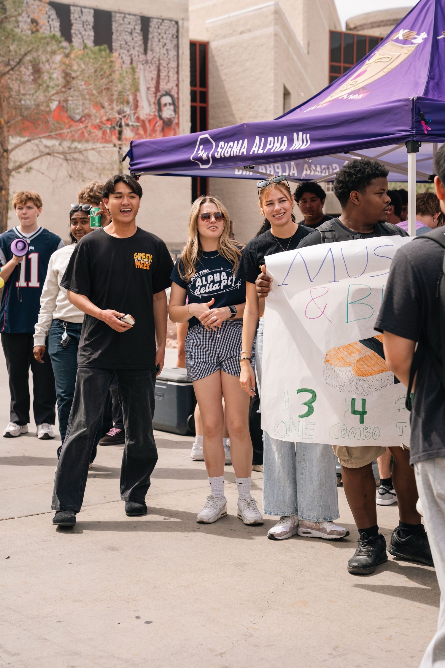 Students gathered around purple tent at outdoor campus event.