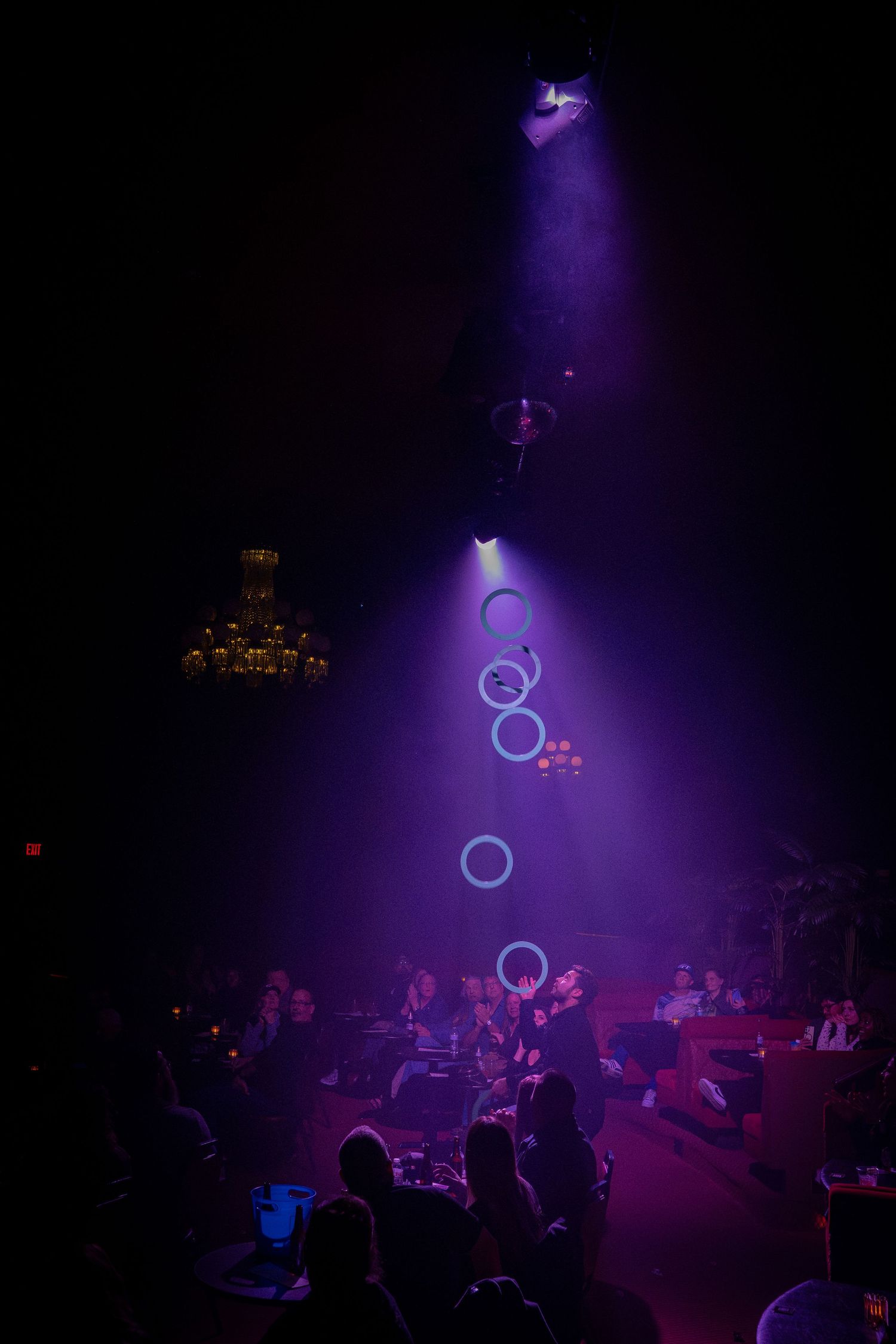 Juggler performs with illuminated rings under purple spotlights on dark stage.