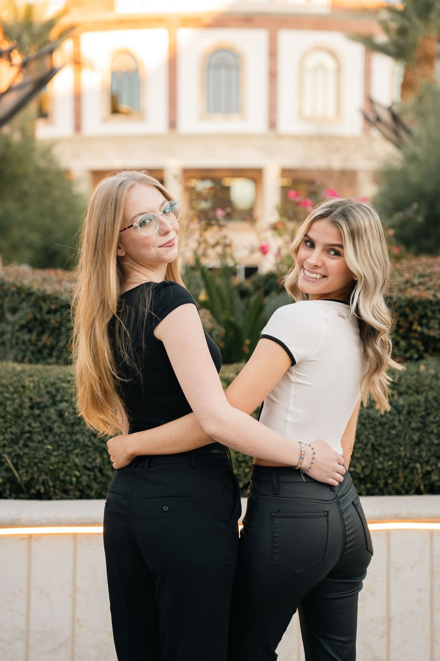 Two friends in black and white outfits pose together against a garden backdrop.