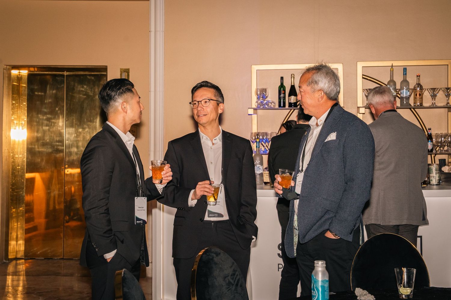 Three professionals engaged in casual conversation at an evening business networking event.