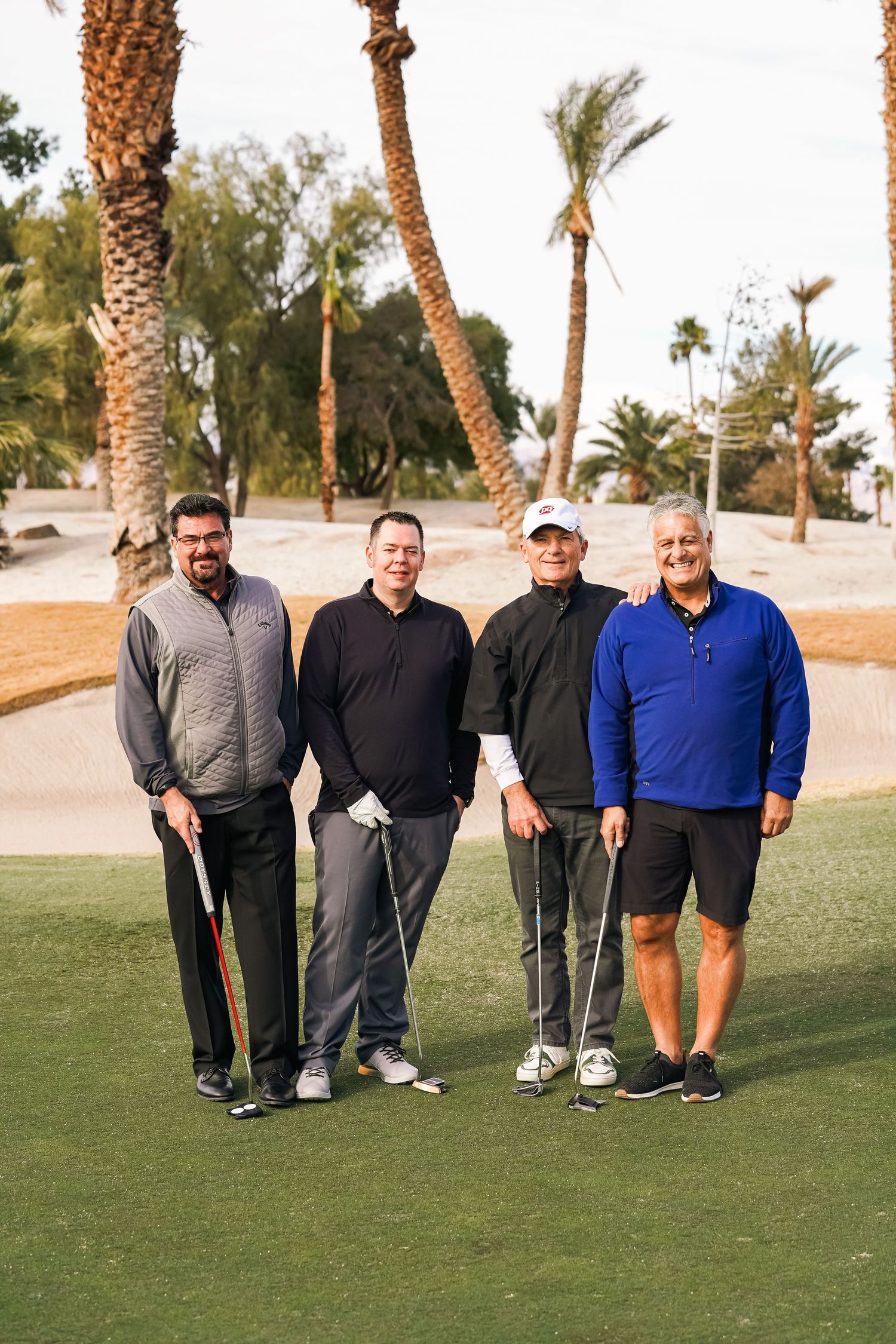 Group of golfers standing together on a green golf course with palm trees in the background.