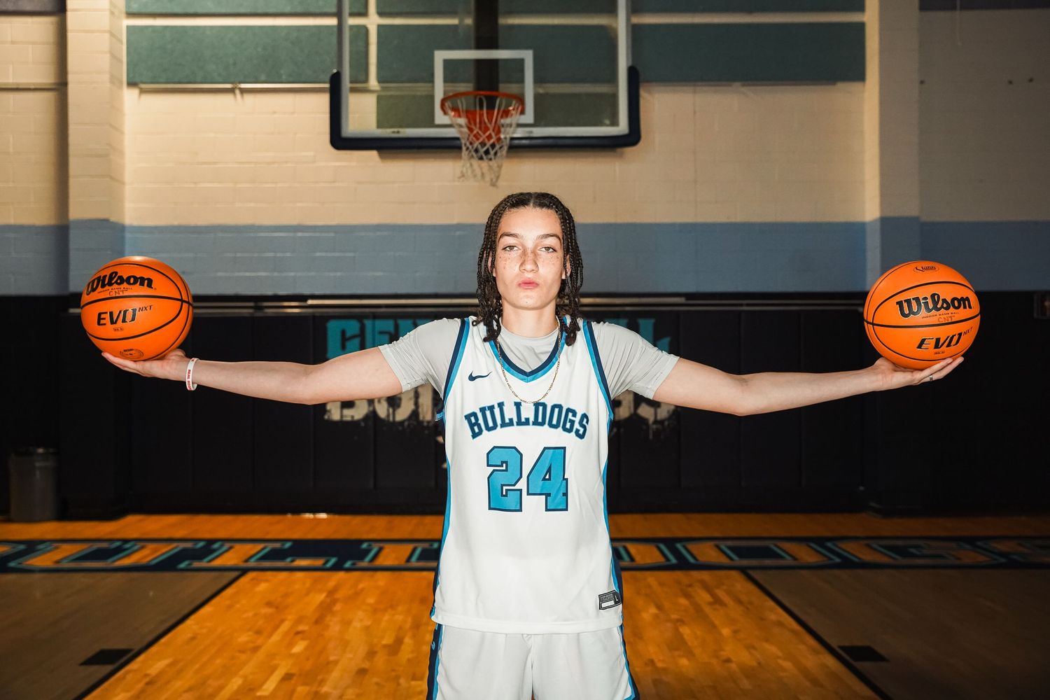 Basketball player in white Bulldogs jersey number 24 poses with two basketballs in gymnasium.
